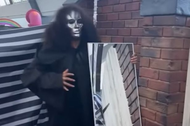 A woman in a silver mask holds a mirror.