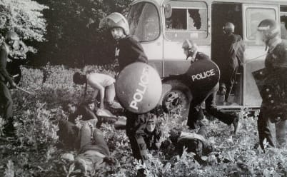 Police in riot gear and Travellers clash outside of a van with broken windows at the Battle of the Beanfield.