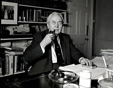 Harold Wilson, former British Prime Minister, sitting at his desk smoking his pipe. 