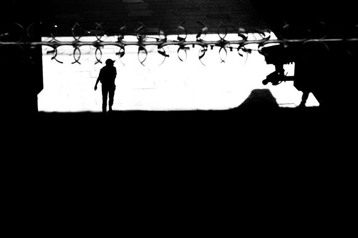 black and white: a man in a baseball cap is seen below some barbed wire and a CCTV camera