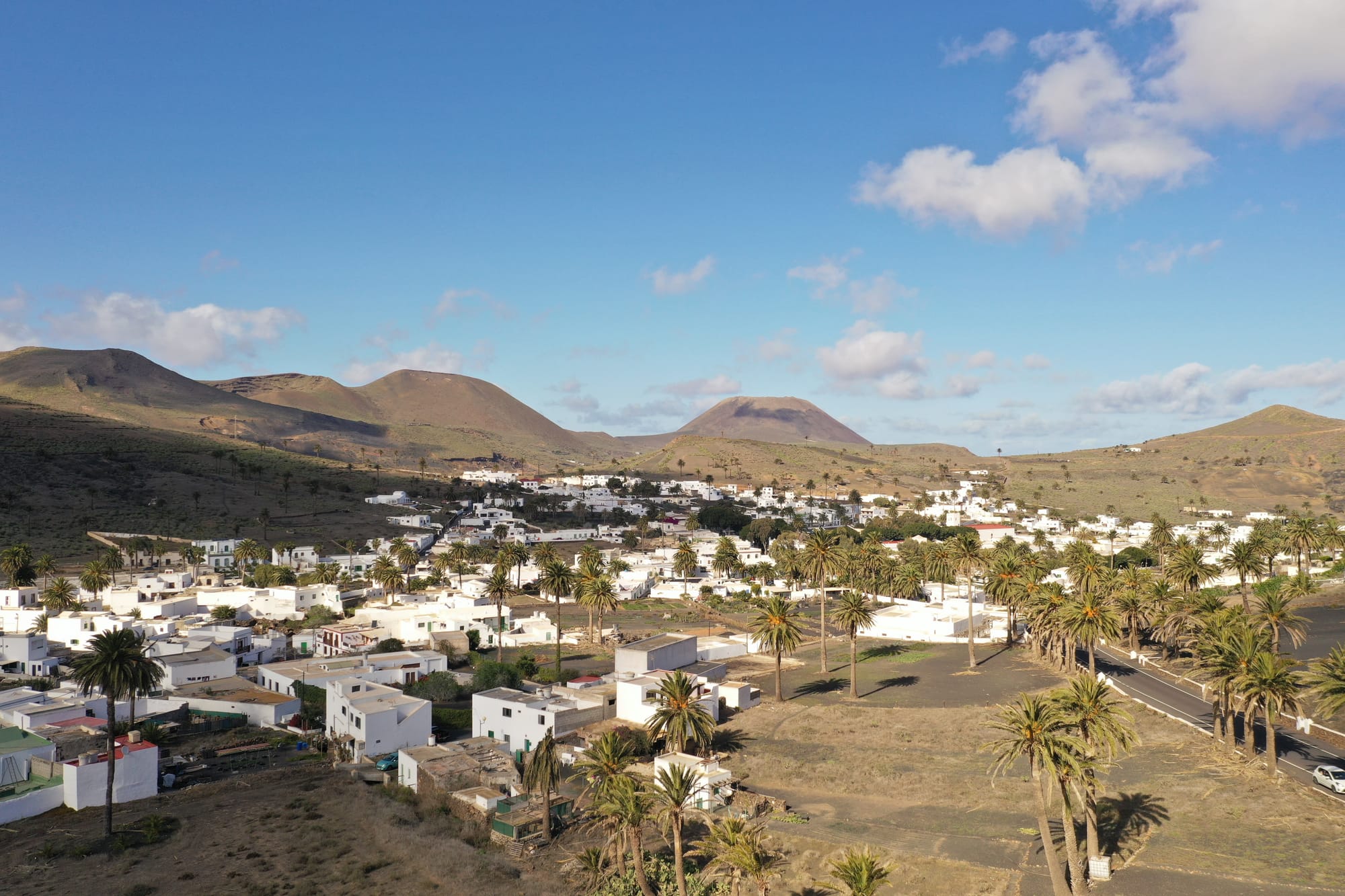Aerial view of Teguise village with white buildings scattered across volcanic landscape and mountains in the background — Lanzarote