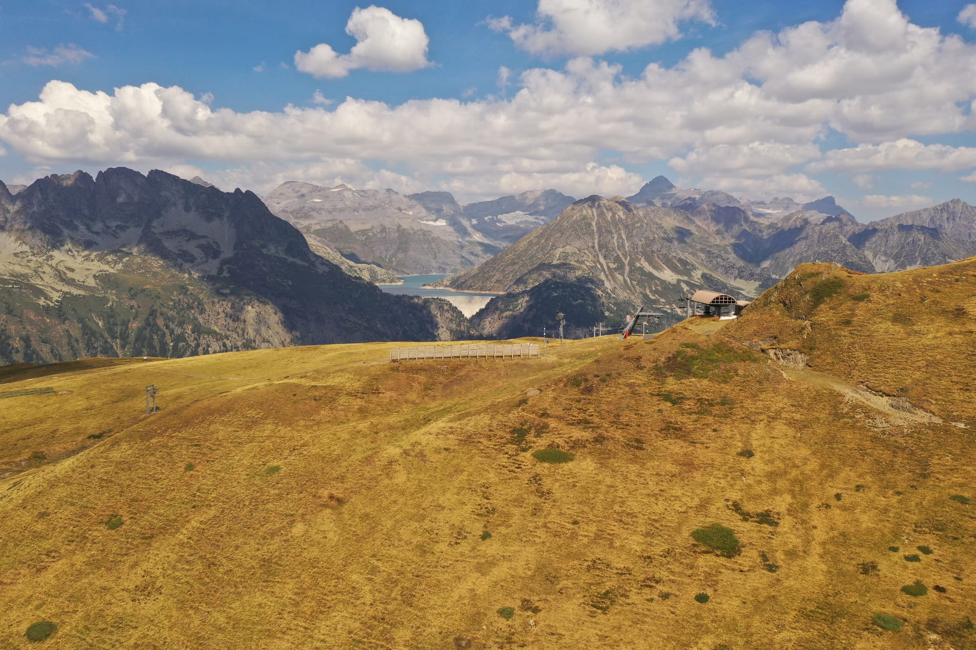 Aerial view of golden alpine meadows with a distant reservoir lake and mountain ridges on the horizon, captured with a DJI Mavic Pro 2 — Saint-Gervais area, France