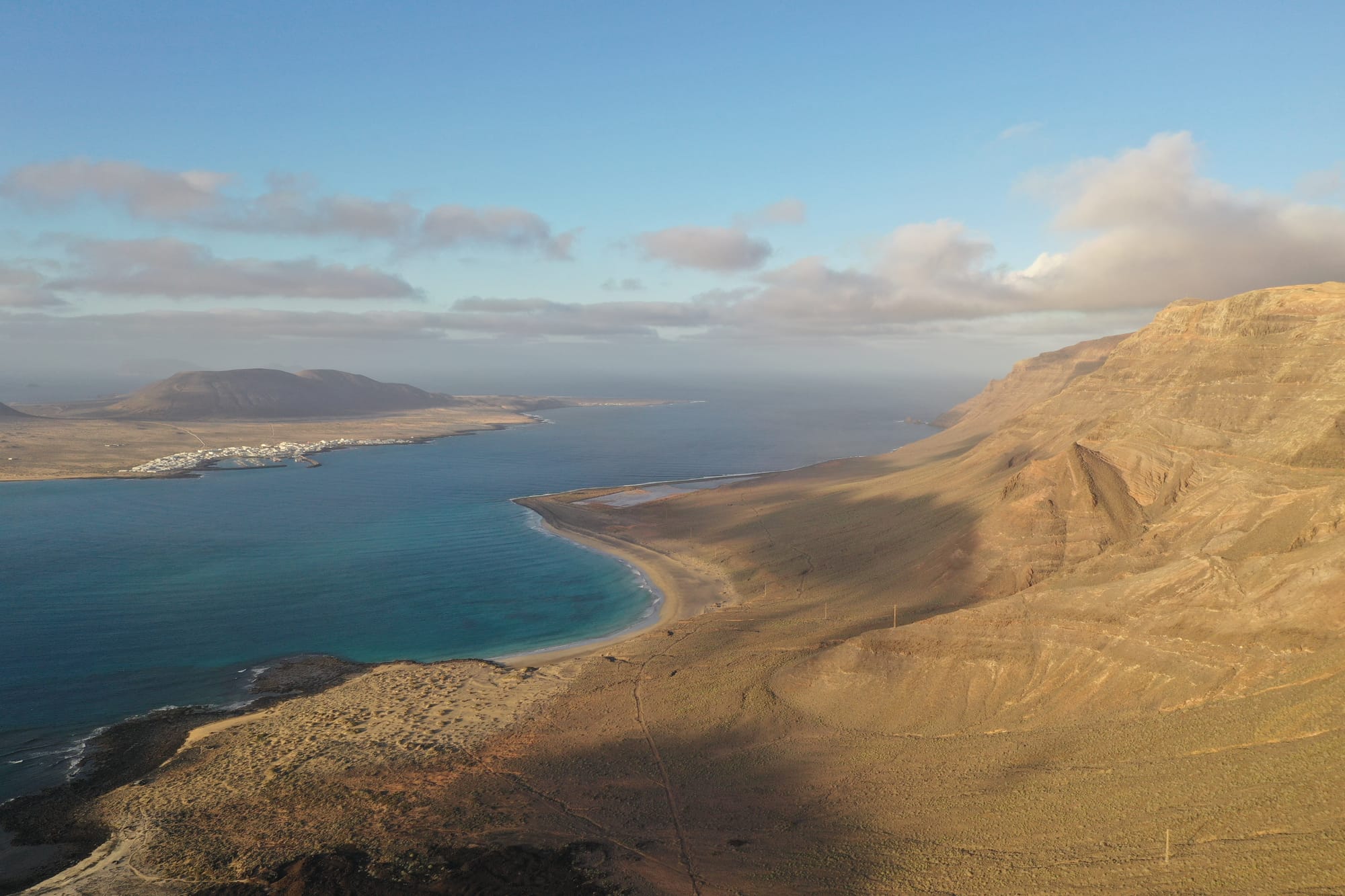Aerial drone view of the Famara coastline and La Graciosa island at golden hour, with turquoise waters and the desert-like landscape glowing in warm light — Lanzarote