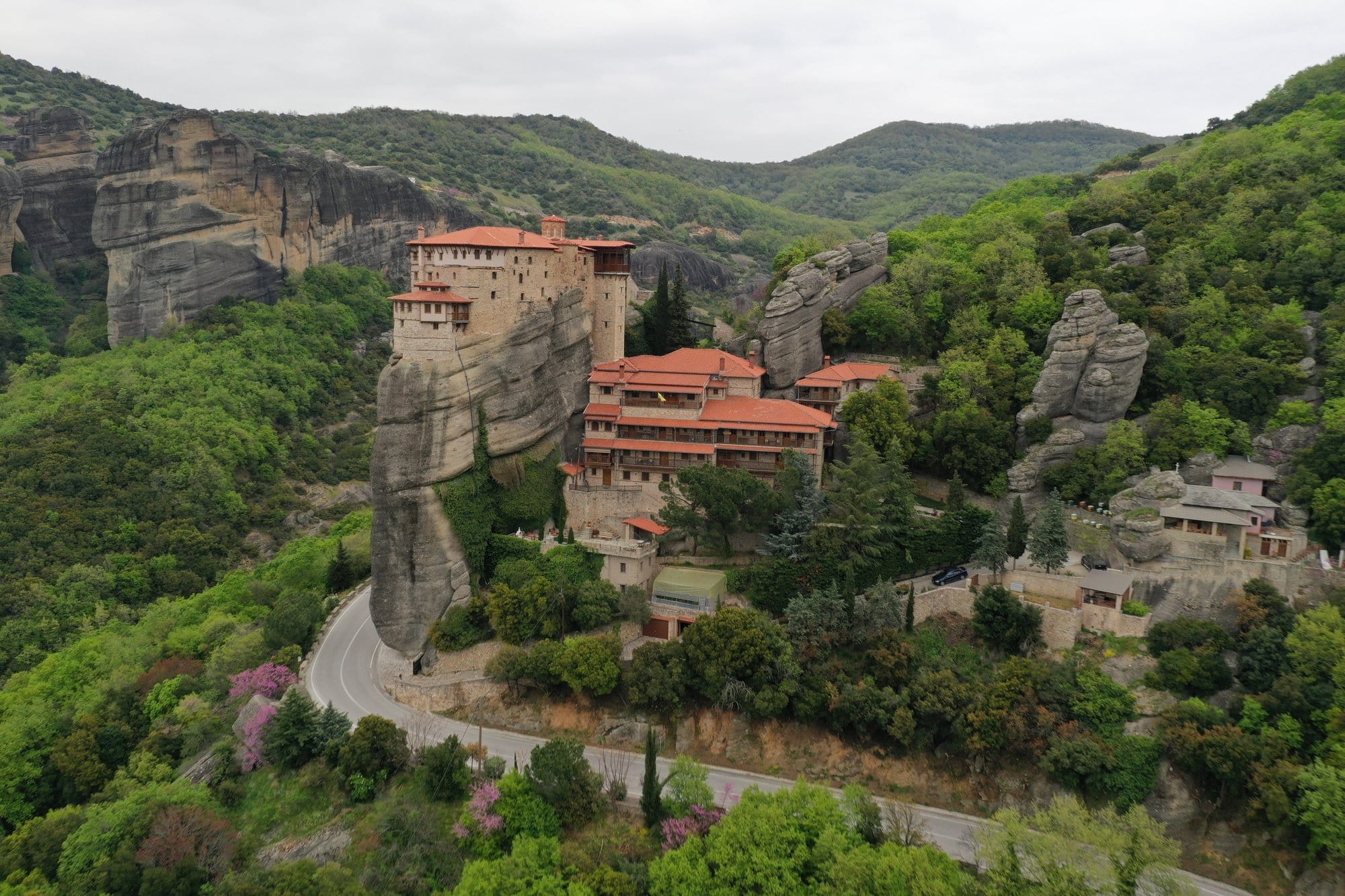 Drone view of a switchback road climbing towards a Meteora monastery — Greece