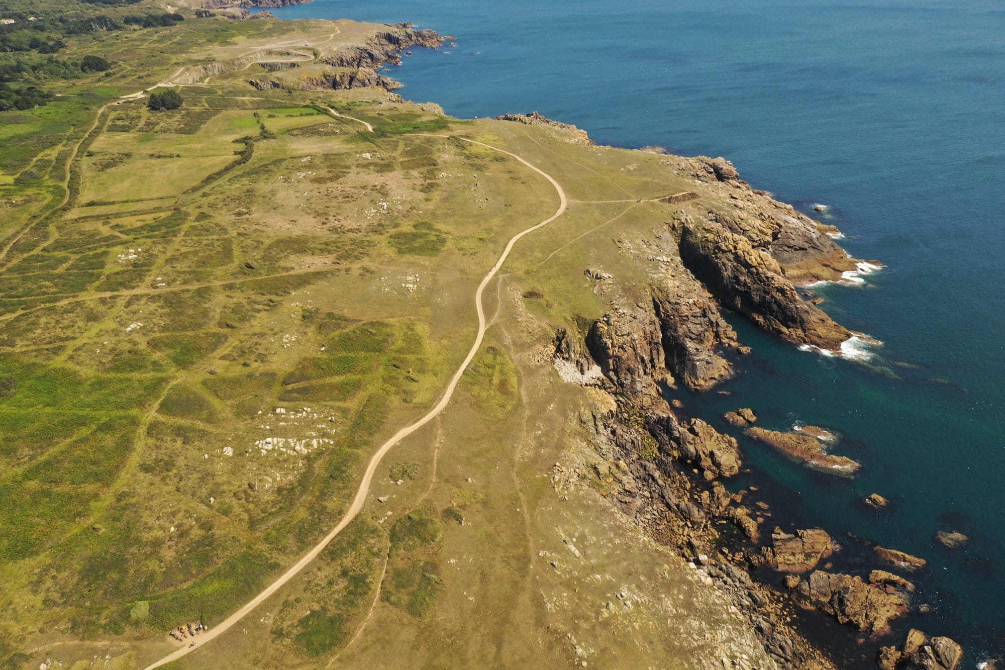 Aerial view of the winding coastal path along the Côte Sauvage, low heath and rugged cliffs dropping into the deep blue Atlantic, captured with a DJI Mavic Pro 2 — Île d'Yeu, France