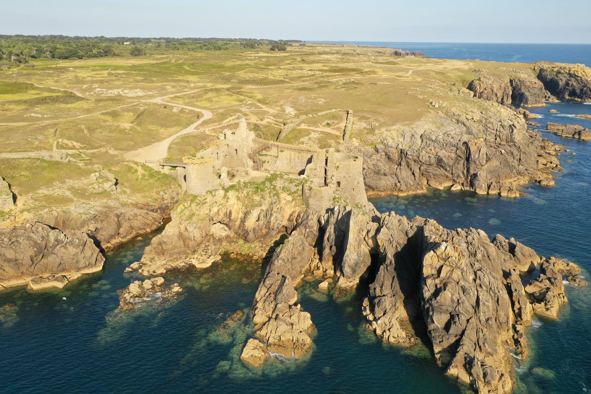 The Vieux-Château ruins seen from the west, dramatic rocky cliffs and fortified walls catching the golden evening light, captured with a DJI Mavic Pro 2 — Île d'Yeu, France