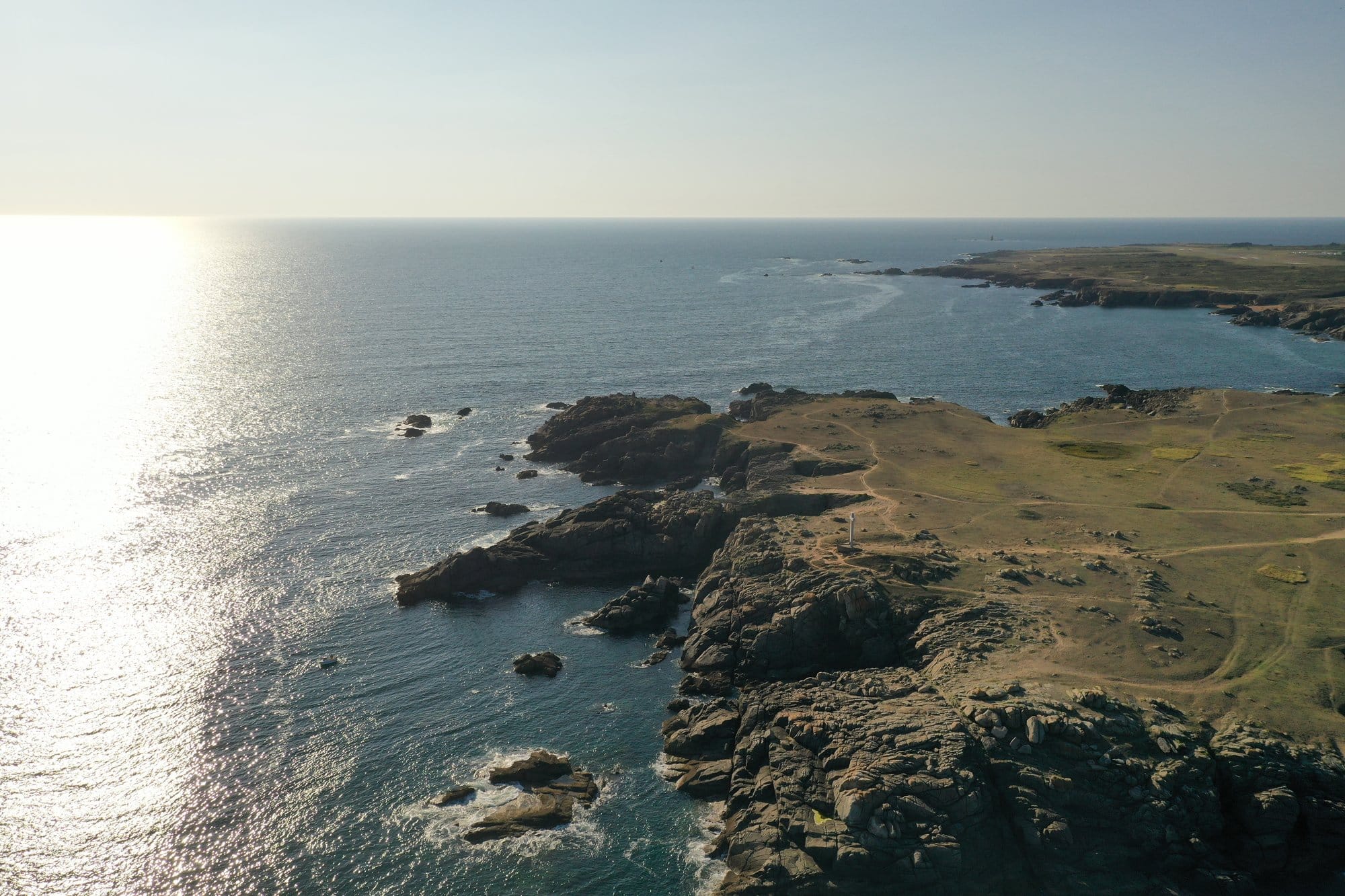 Aerial view of the Côte Sauvage at golden hour, the sun's reflection shimmering across the Atlantic surface, captured with a DJI Mavic Pro 2 — Île d'Yeu, France