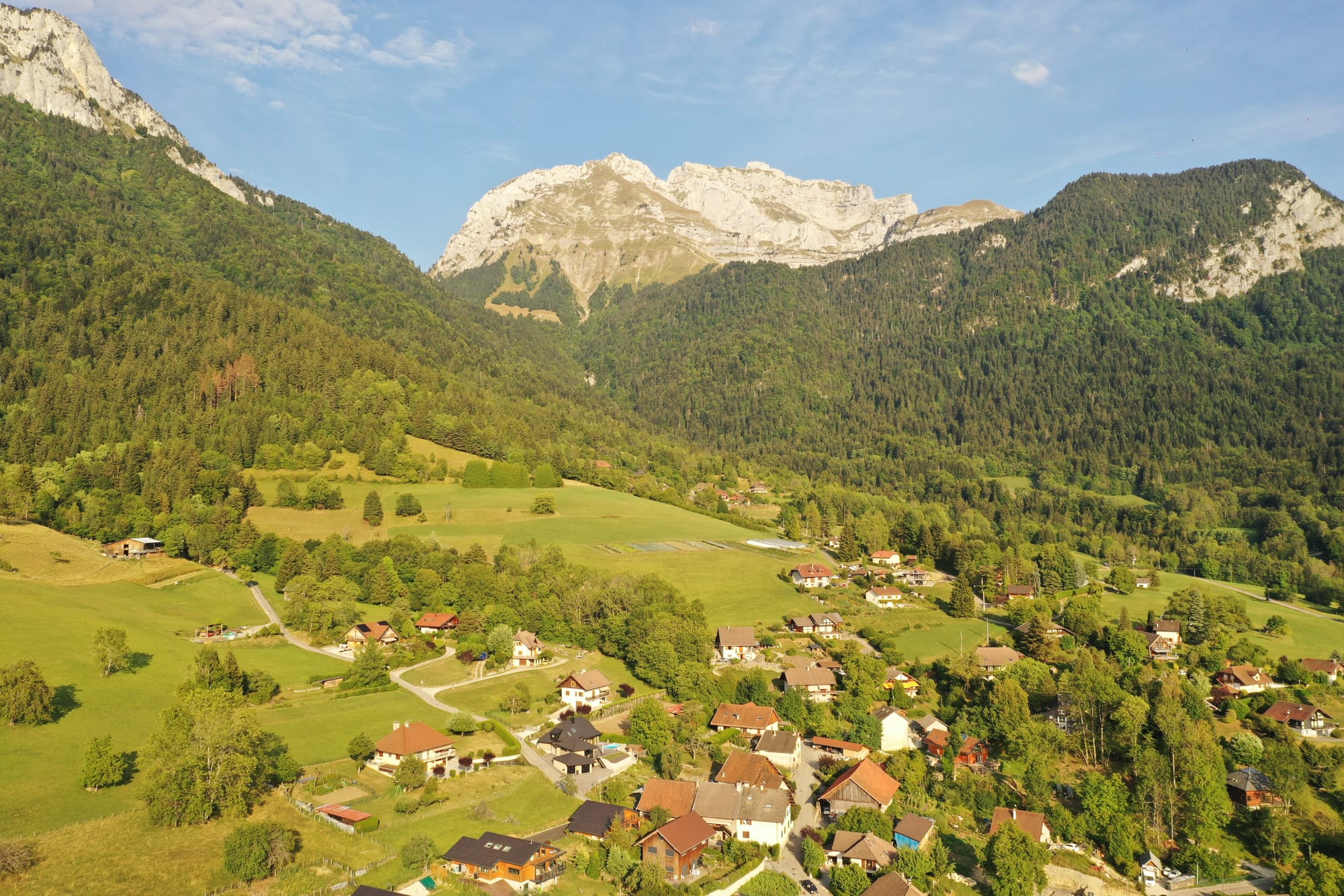 Aerial view of a picturesque alpine village with red rooftops nestled in a green valley beneath imposing limestone mountains, captured with a DJI Mavic Pro 2 — French Alps, France