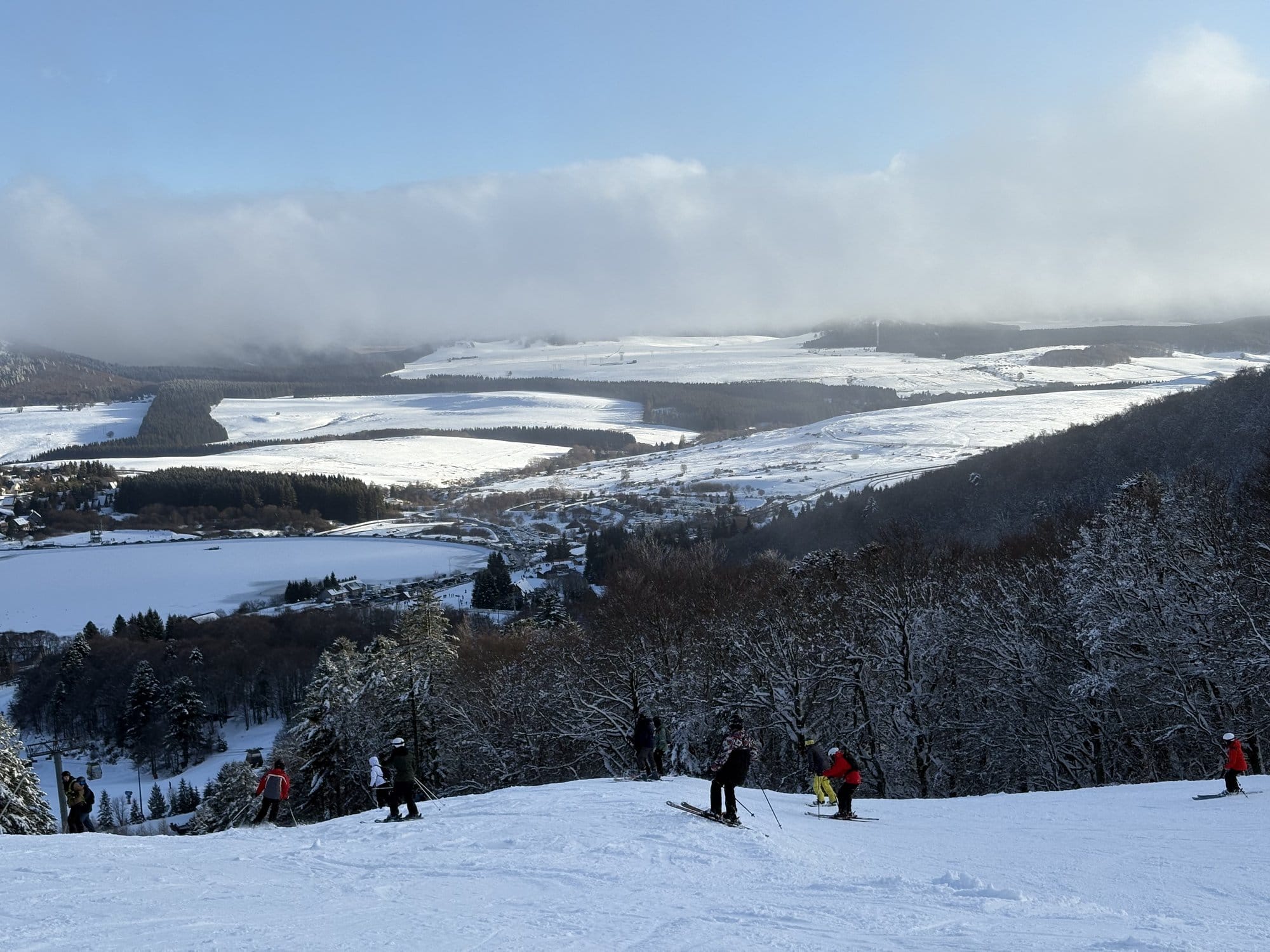 Skiers on the slopes of Super Besse with panoramic views across the snow-covered Auvergne plateau — Auvergne, France