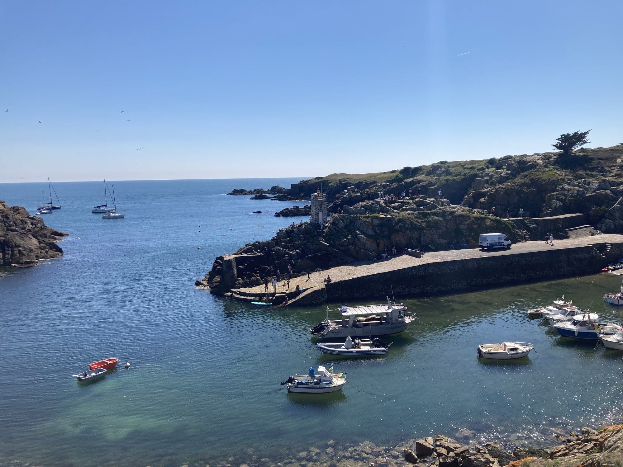 Port de la Meule harbour seen from the clifftop path, boats moored along the stone jetty with clear waters below — Île d'Yeu, France