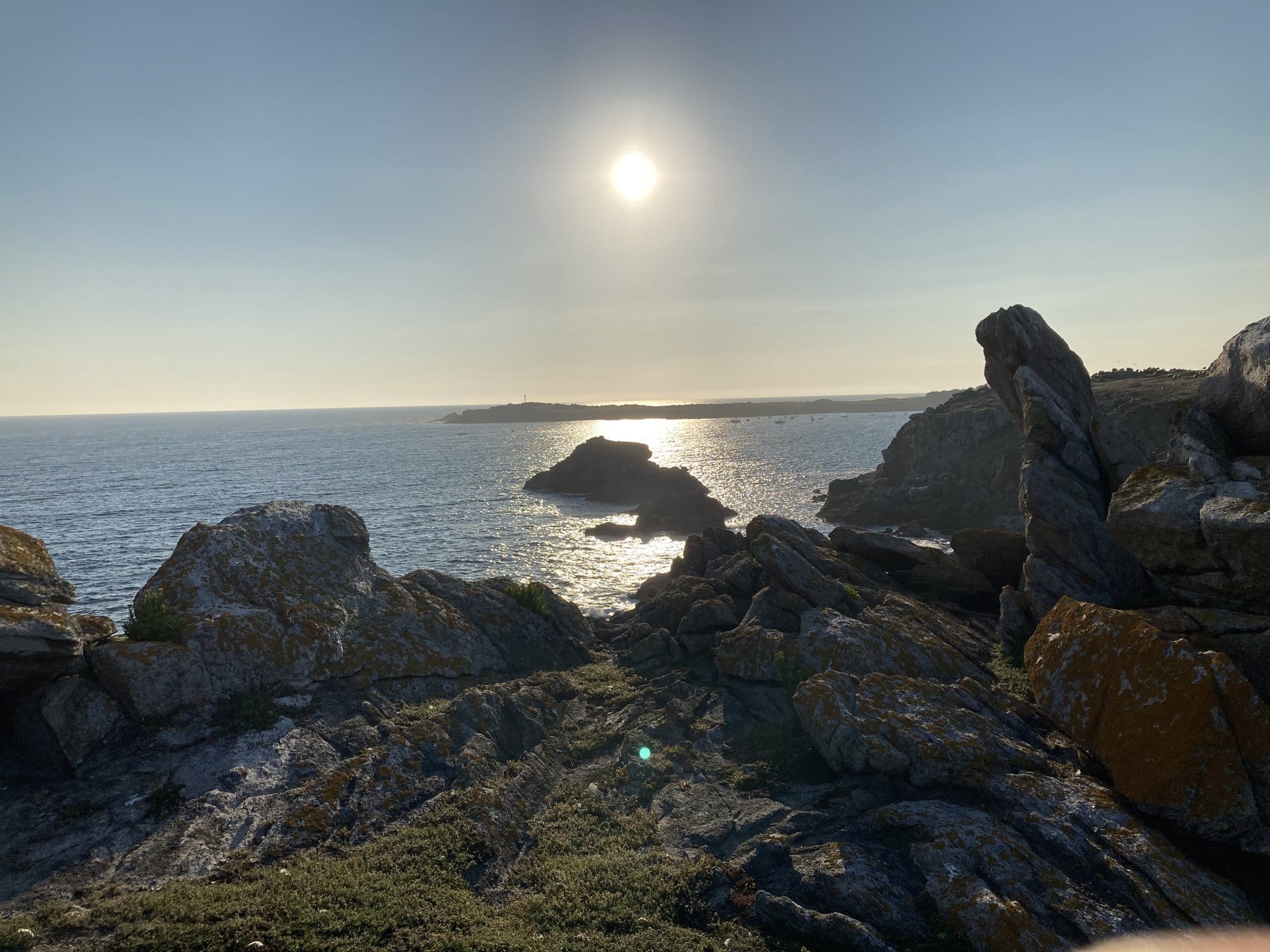 Rocky coastline of the Côte Sauvage at sunset, warm light on granite boulders with the sun low over the Atlantic horizon — Île d'Yeu, France