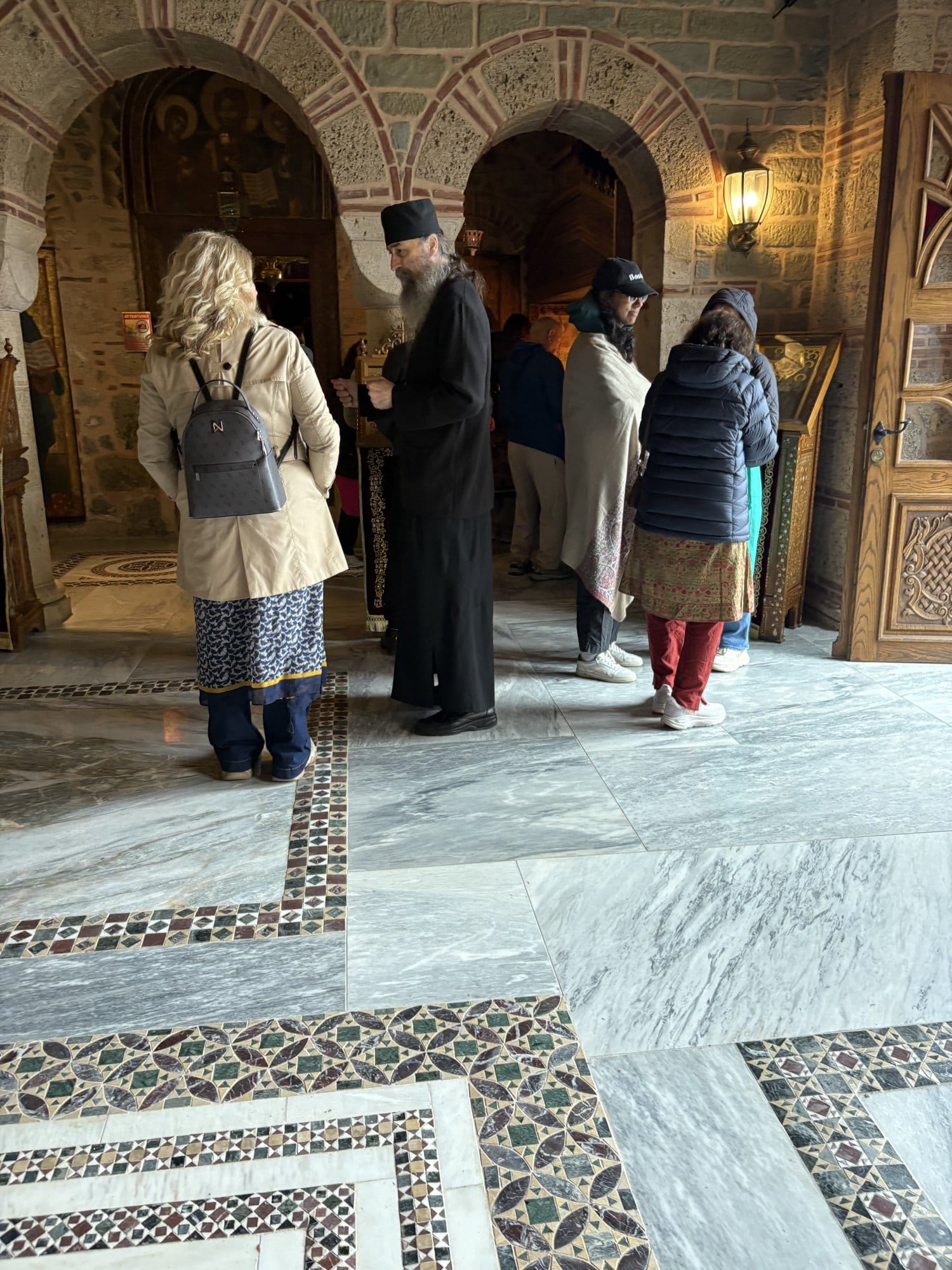 Un moine en robe noire s'entretient avec des visiteurs dans une salle d'un monastère de Meteora — Grèce