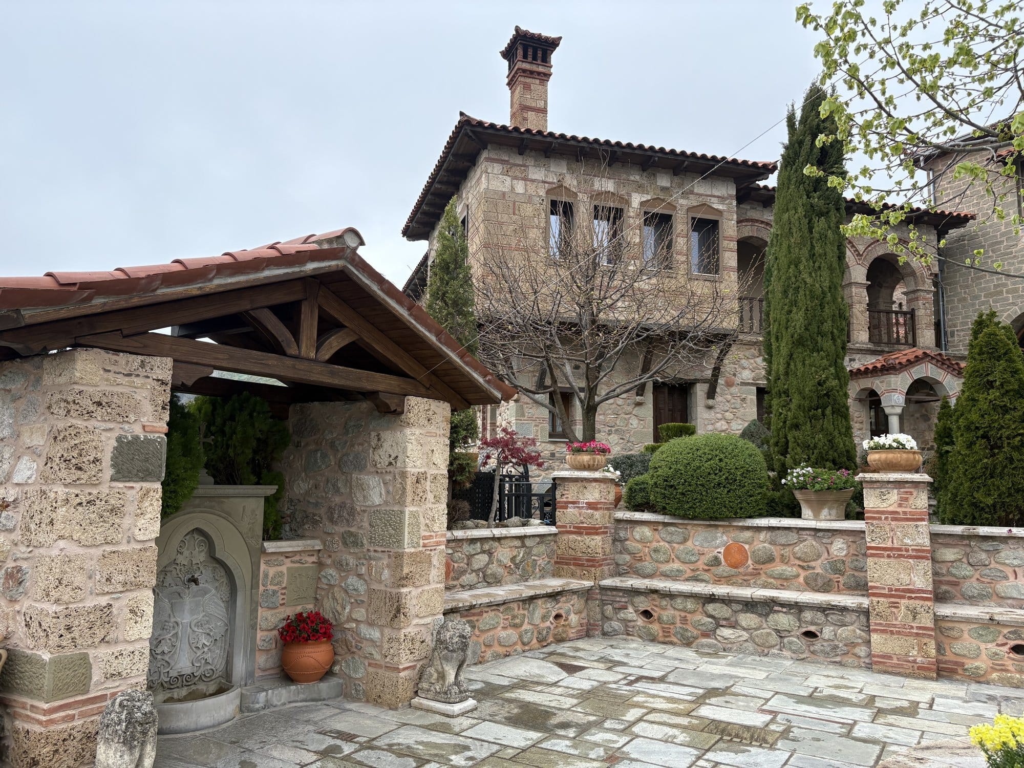 Stone monastery courtyard with well, flower pots and tiled roofs — Meteora, Greece