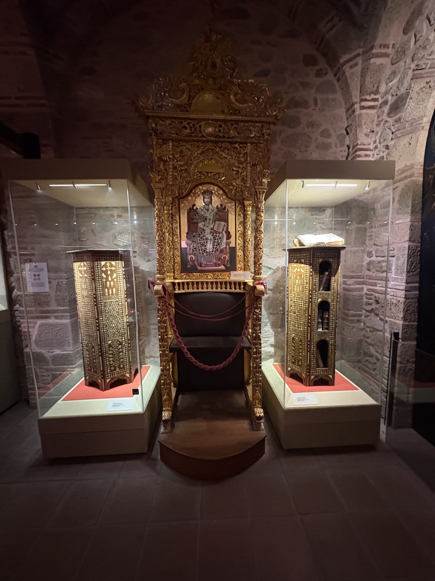 Ornate gilded wooden throne and display cases inside a Meteora monastery treasury — Greece