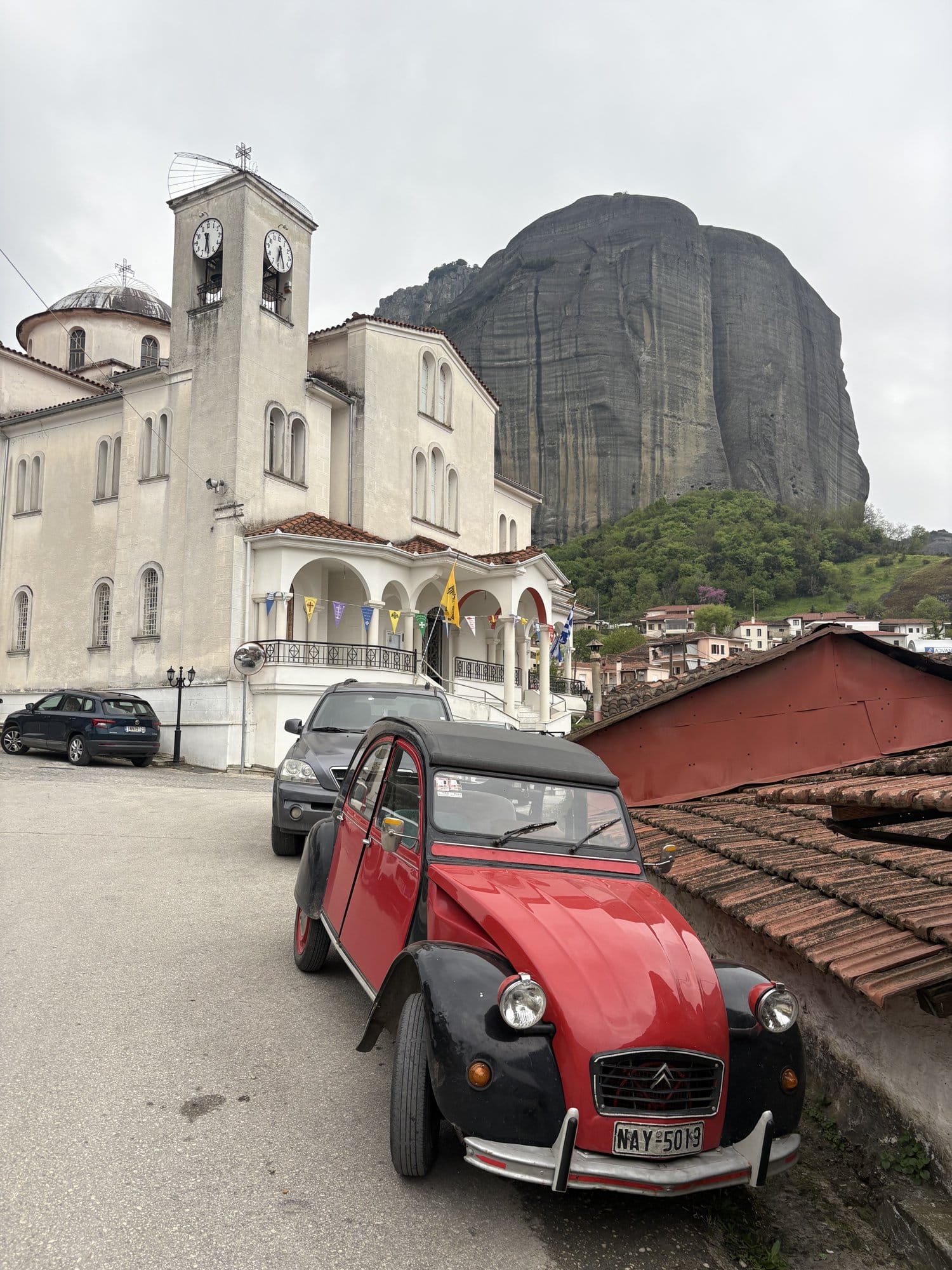 White Greek church with bell tower, red Citroën 2CV parked in front and Meteora rock behind — Kastraki, Greece