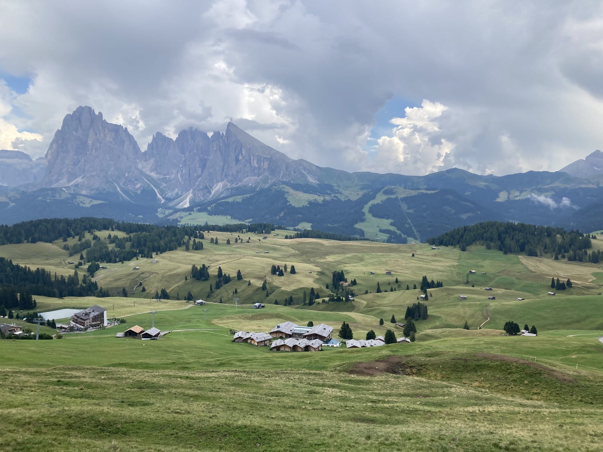 Panoramic view of Alpe di Siusi with mountain chalets and Sassolungo in the background โ Dolomites, Italy