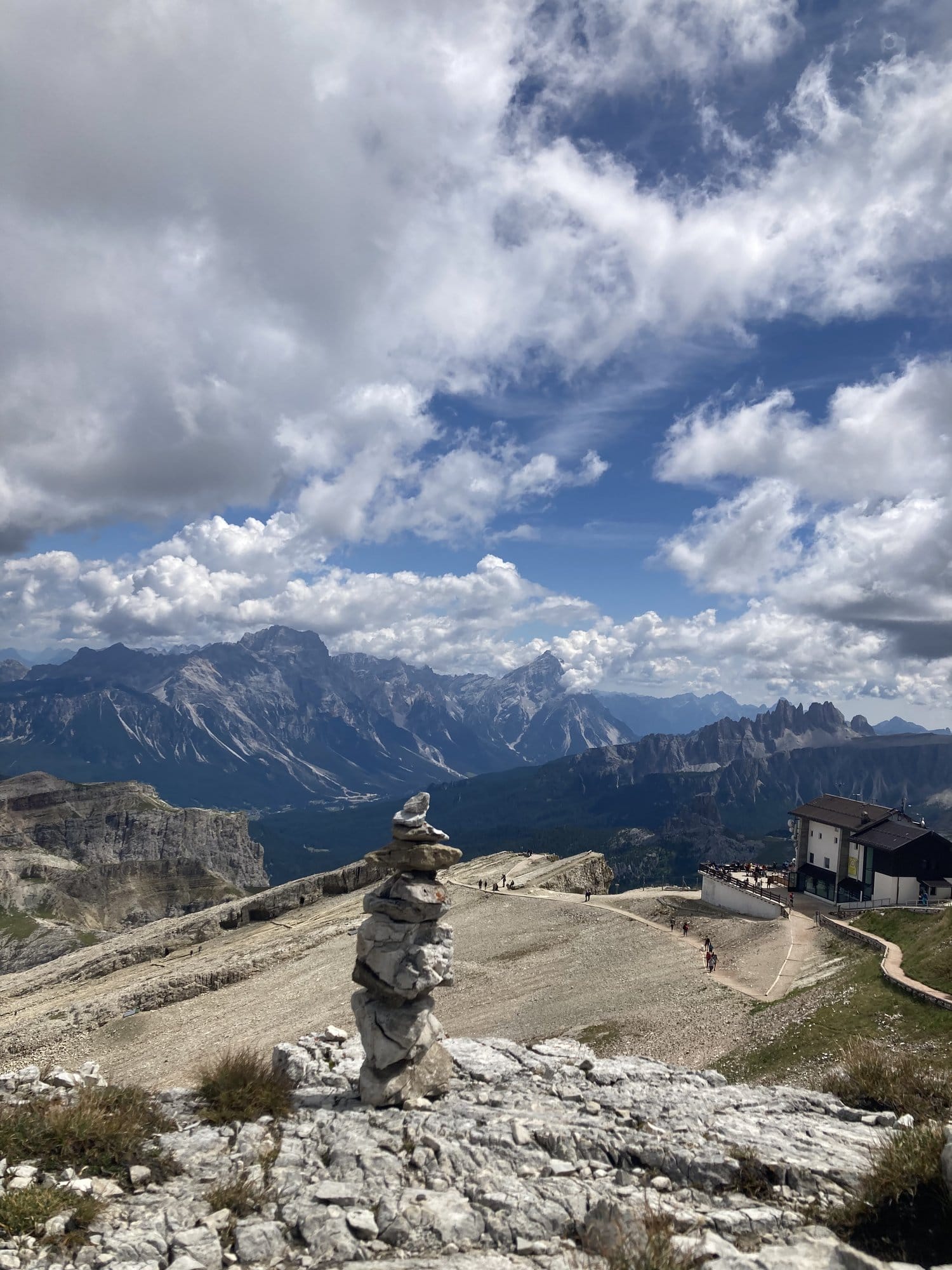 Stone cairn at Lagazuoi summit with panoramic Dolomite views and Rifugio Lagazuoi — Dolomites, Italy