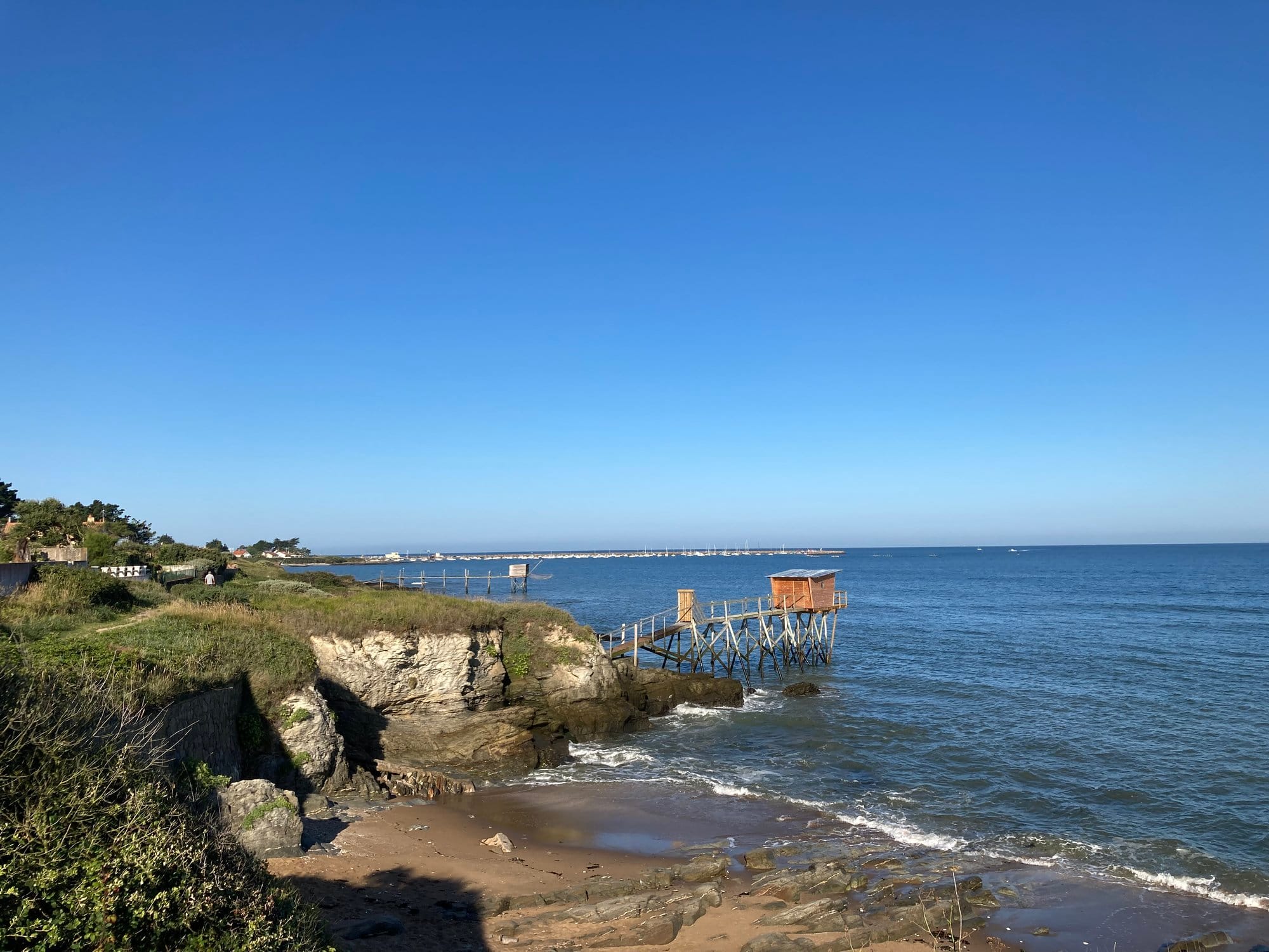 Pornic coastal path with white cliffs and traditional wooden carrelet pier visible in the background