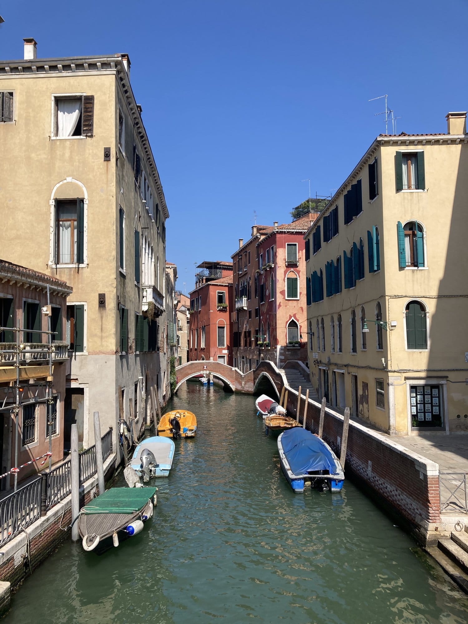 Canal with colorful boats and a stone bridge in the Castello quarter — Venice, Italy