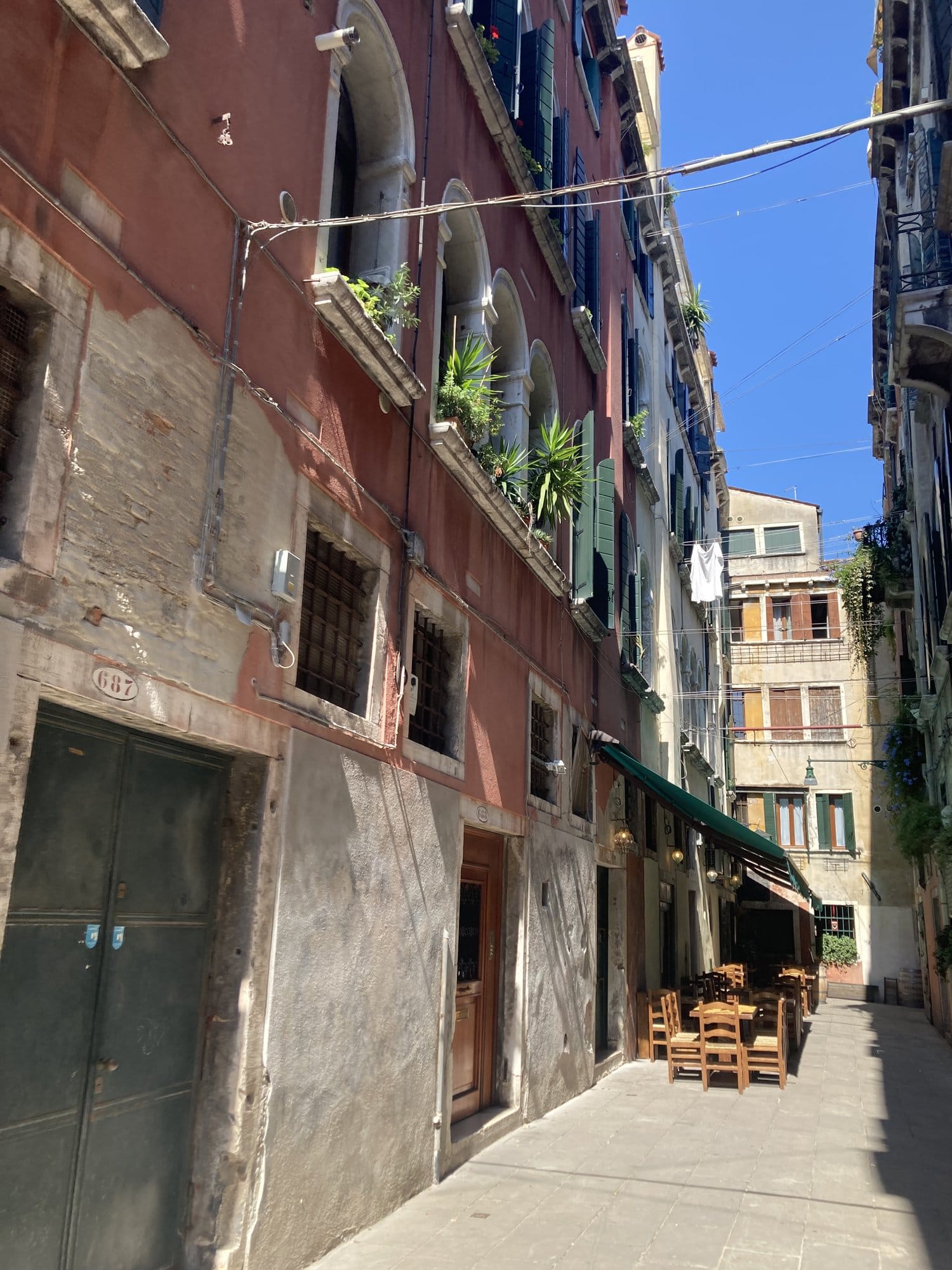 Narrow pedestrian alley with ochre buildings and restaurant terraces — Venice, Italy