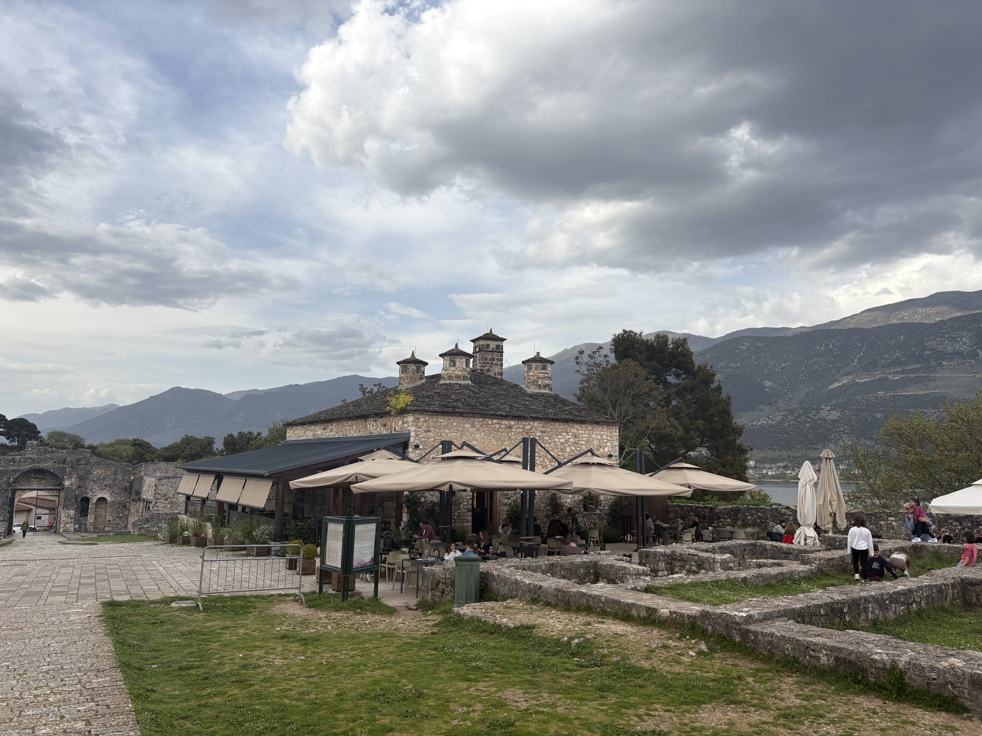 Cour de la citadelle avec bâtiment ottoman, parasols de café et montagne en fond — Ioannina, Grèce
