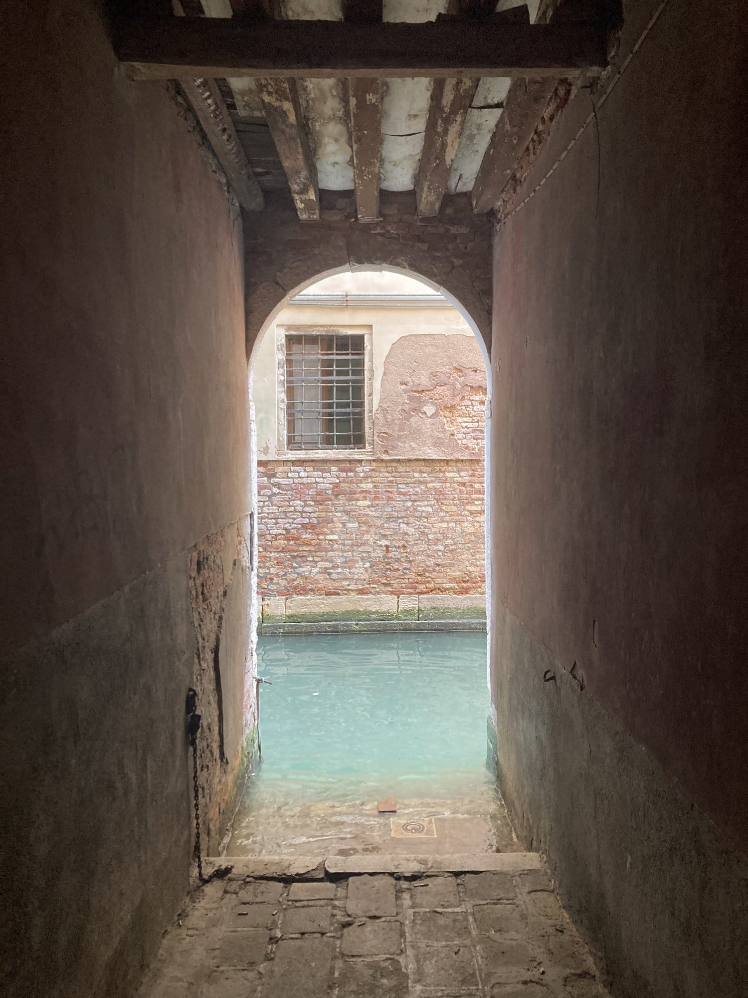 Atmospheric vaulted passage opening onto a turquoise canal — Venice, Italy