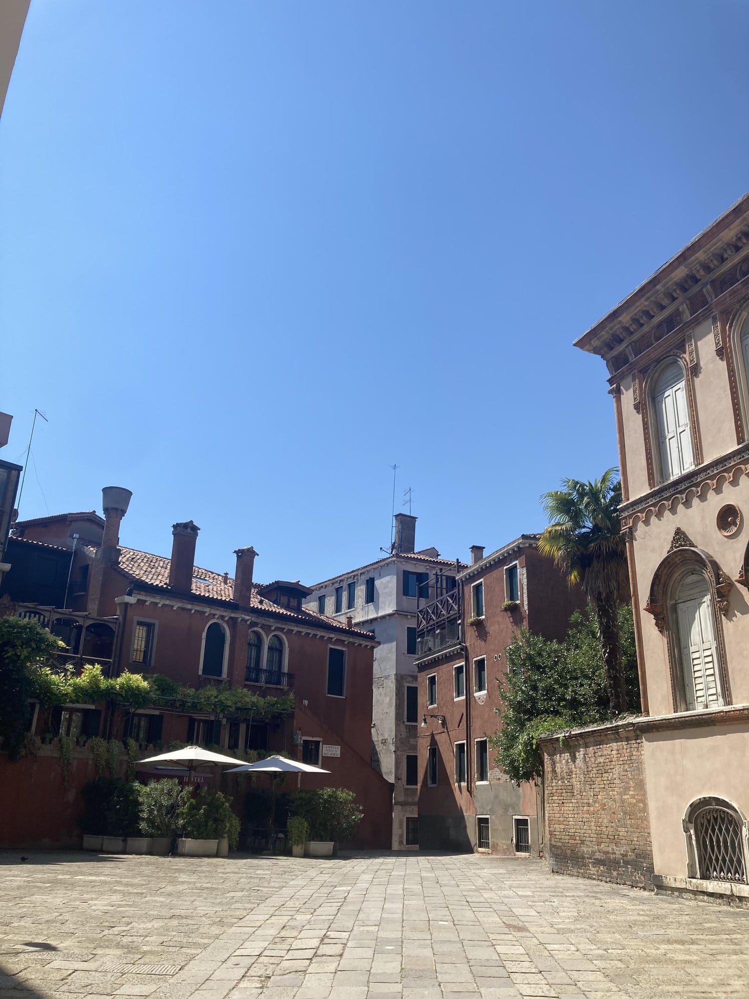 Quiet residential square in Dorsoduro with ochre buildings and a palm tree — Venice, Italy