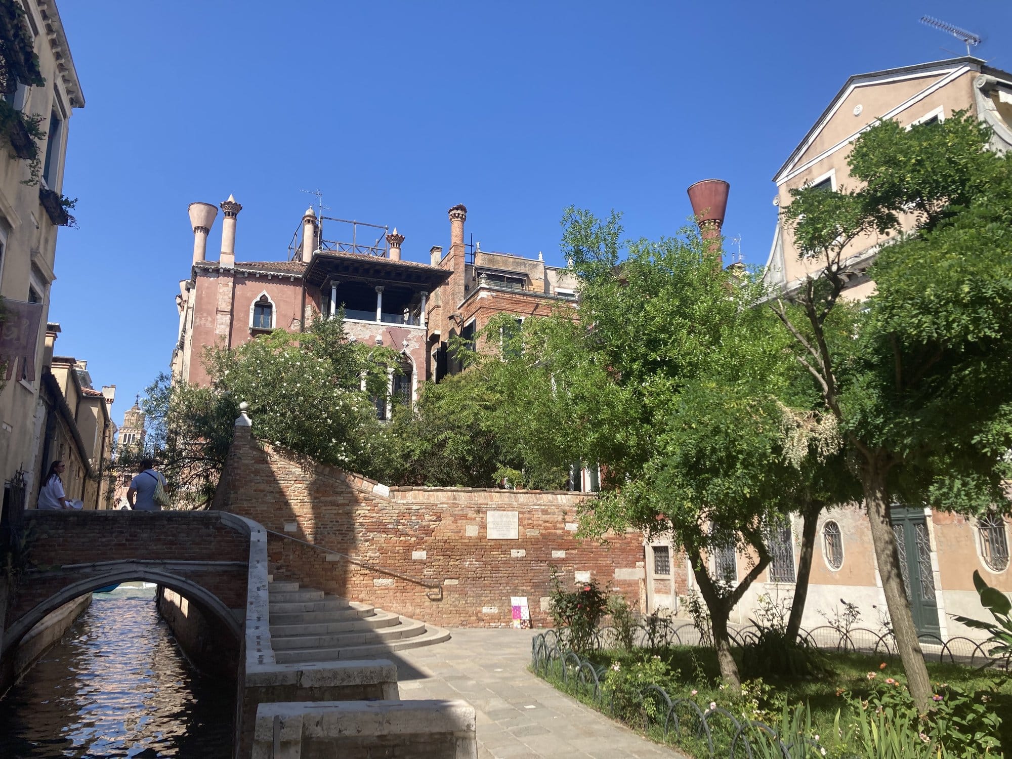 Small bridge over a Dorsoduro canal with lush vegetation and rooftop terraces — Venice, Italy