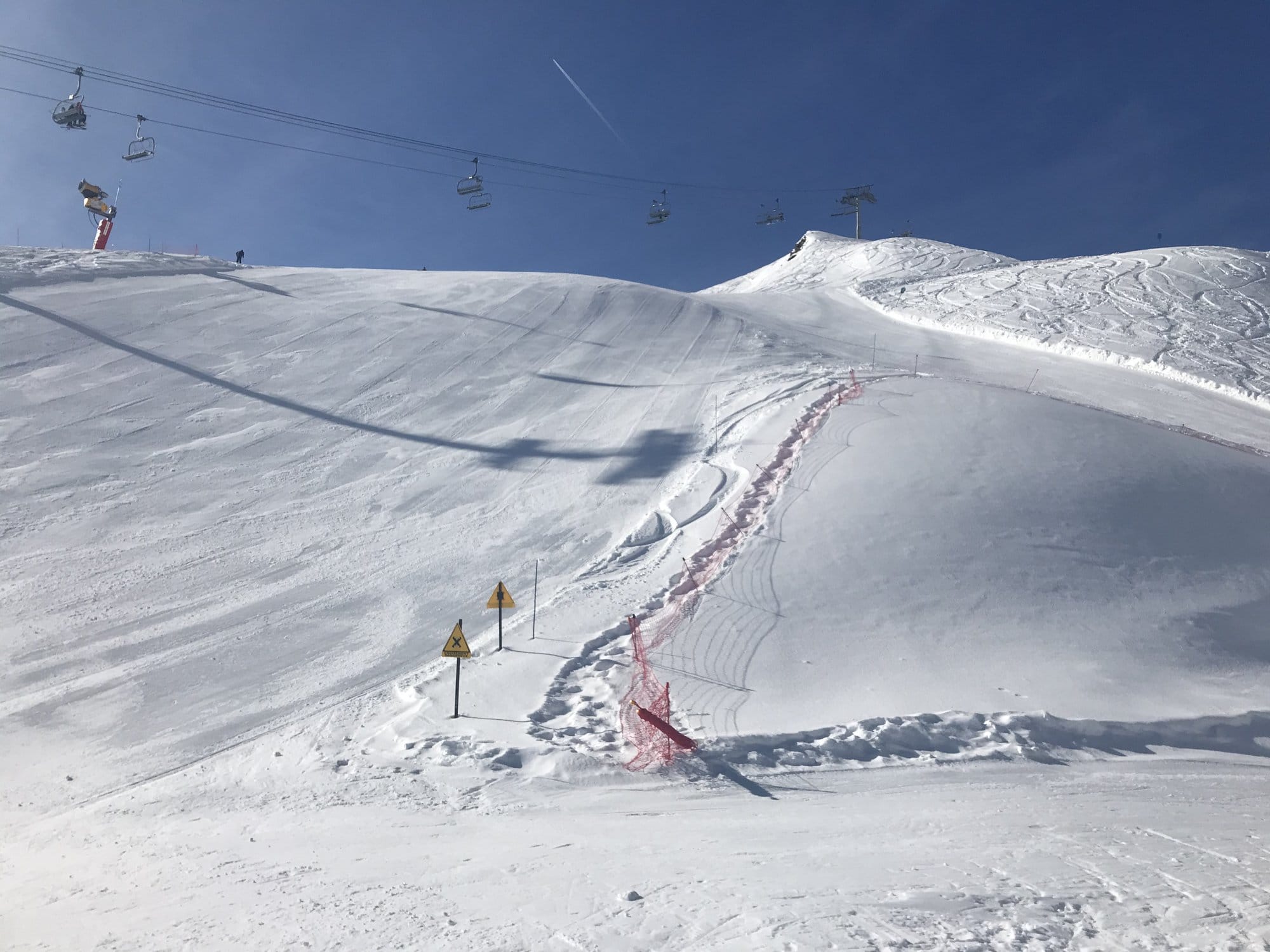 A perfectly groomed ski run at the Cirque du Lys with the chairlift crossing overhead, safety netting and blue sky — Cauterets, France