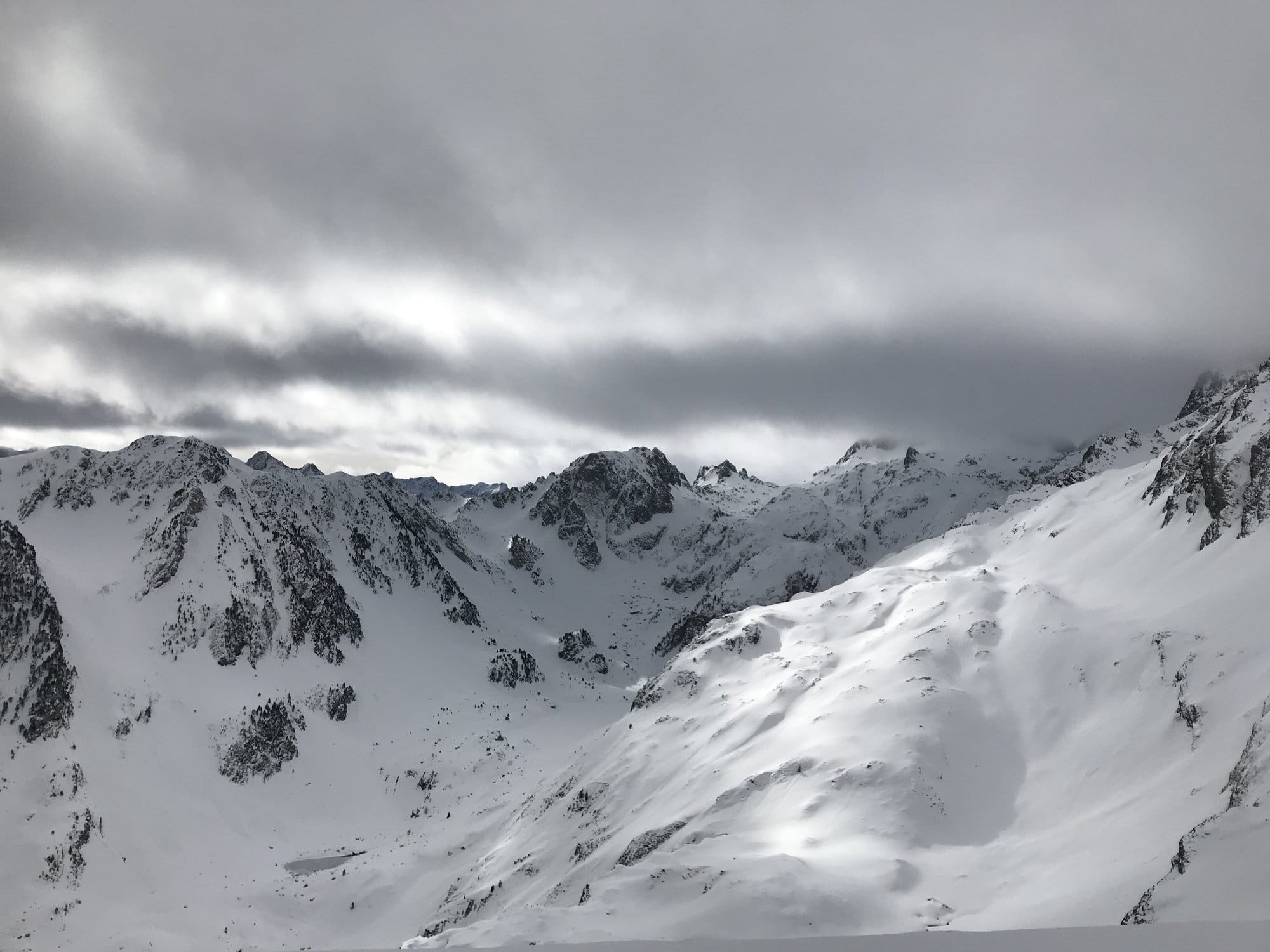The snow-covered Pyrenean peaks seen from the Cirque du Lys under a dramatic overcast sky, with heavy clouds rolling between the ridges — Cauterets, France