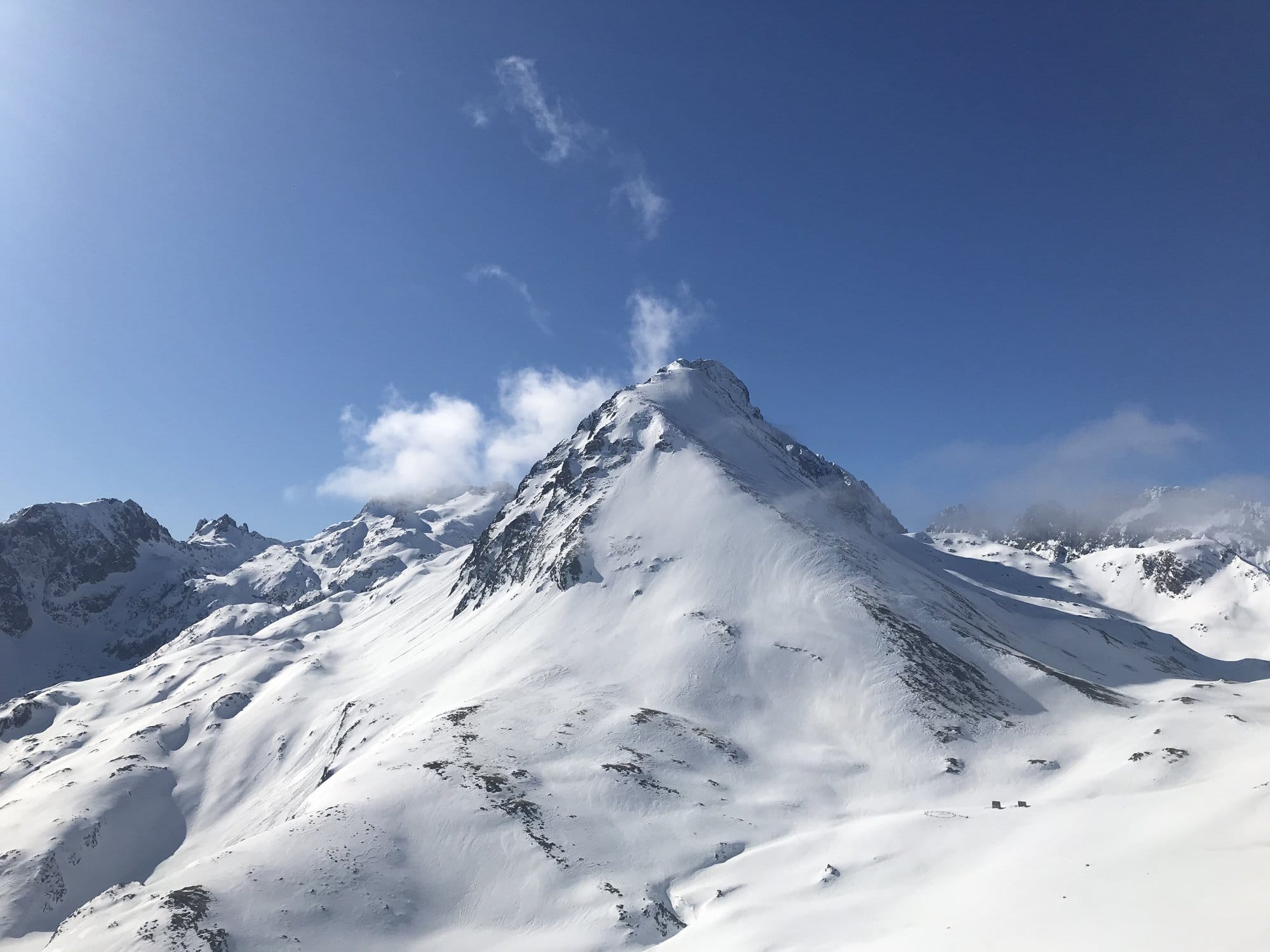 A striking pyramidal Pyrenean peak rising above pristine snowfields under a clear blue sky with wisps of cloud — Cirque du Lys, Cauterets, France