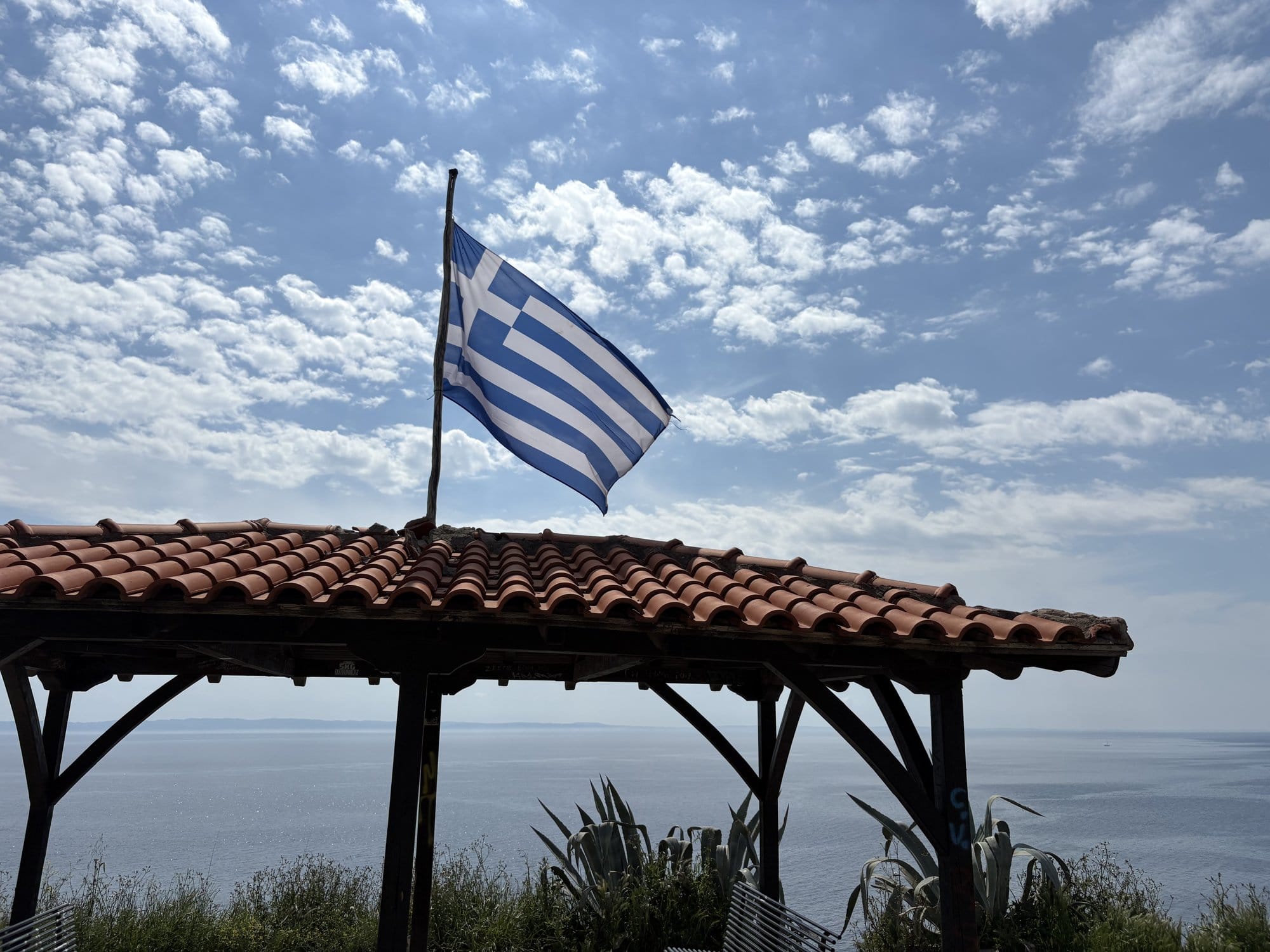 Drapeau grec flottant sur un toit de pergola avec la mer Égée en toile de fond — Parthenonas, Grèce