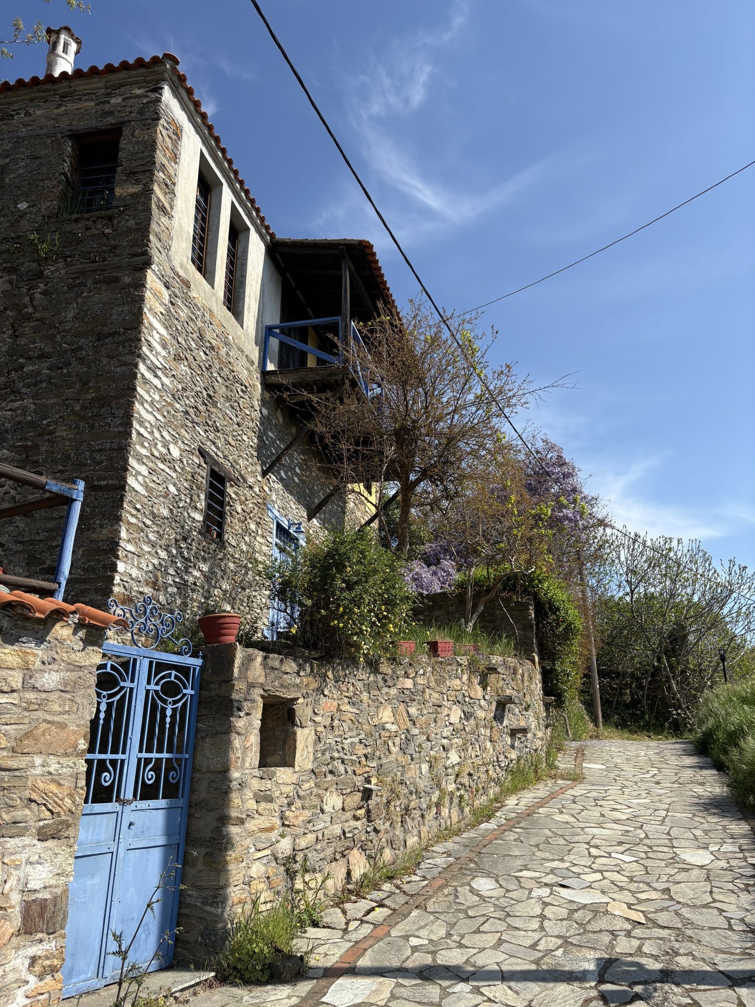 Maison en pierre de Parthenonas avec un portail bleu, de la glycine et une ruelle pavée — Sithonia, Grèce