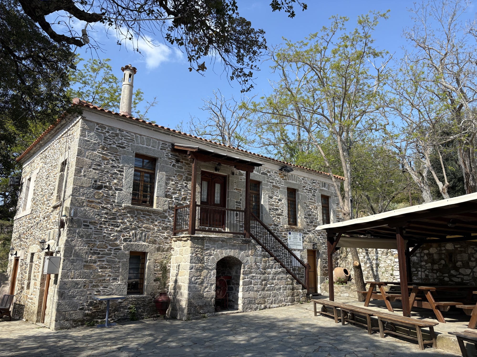 Maison d'hôtes en pierre restaurée dans une ruelle de Parthenonas avec une longue véranda en bois et des murs de pierre — Halkidiki, Grèce