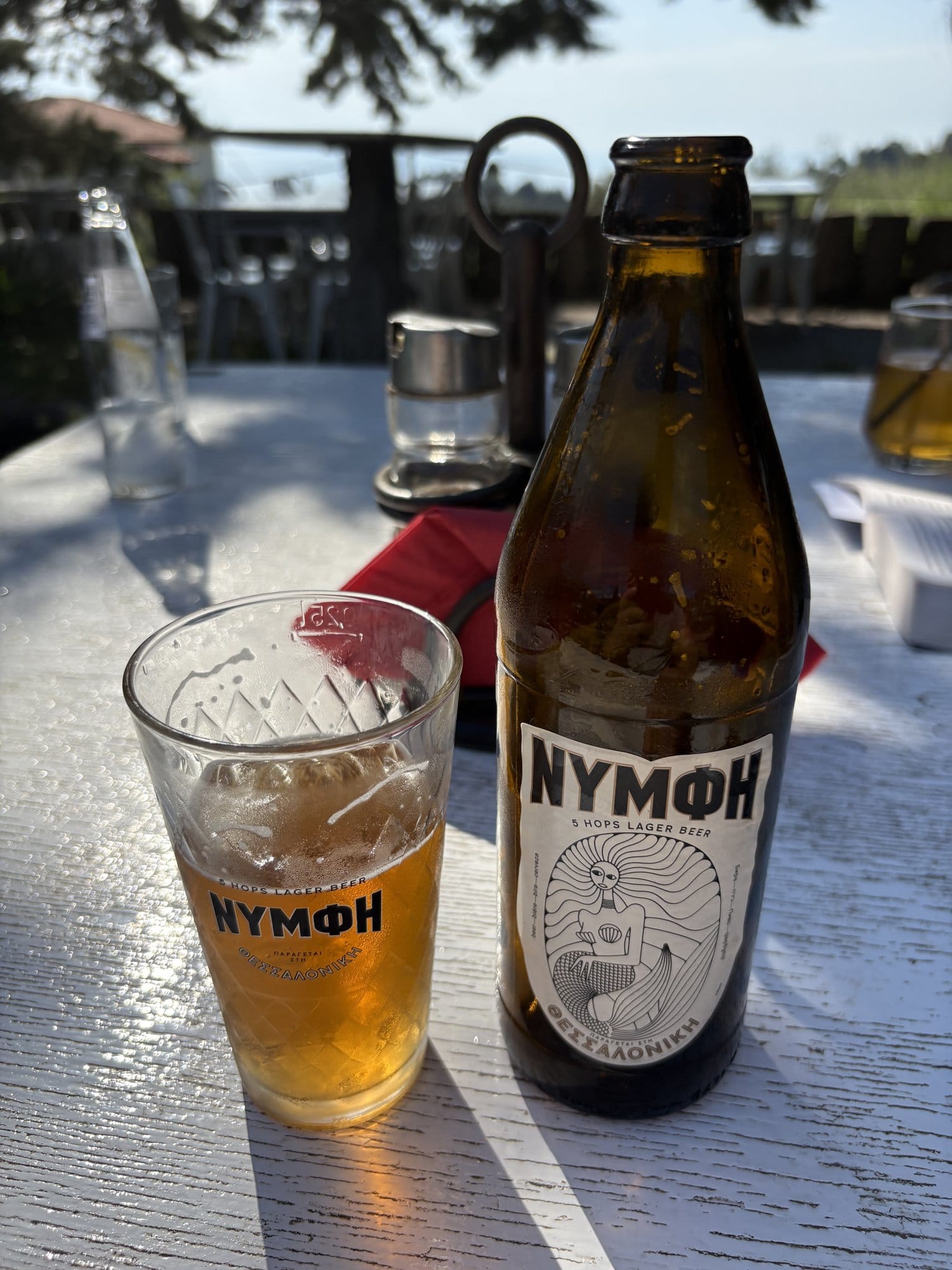 Bouteille et verre de bière grecque Nymph sur une table de taverna à l'heure dorée — Sithonia, Grèce