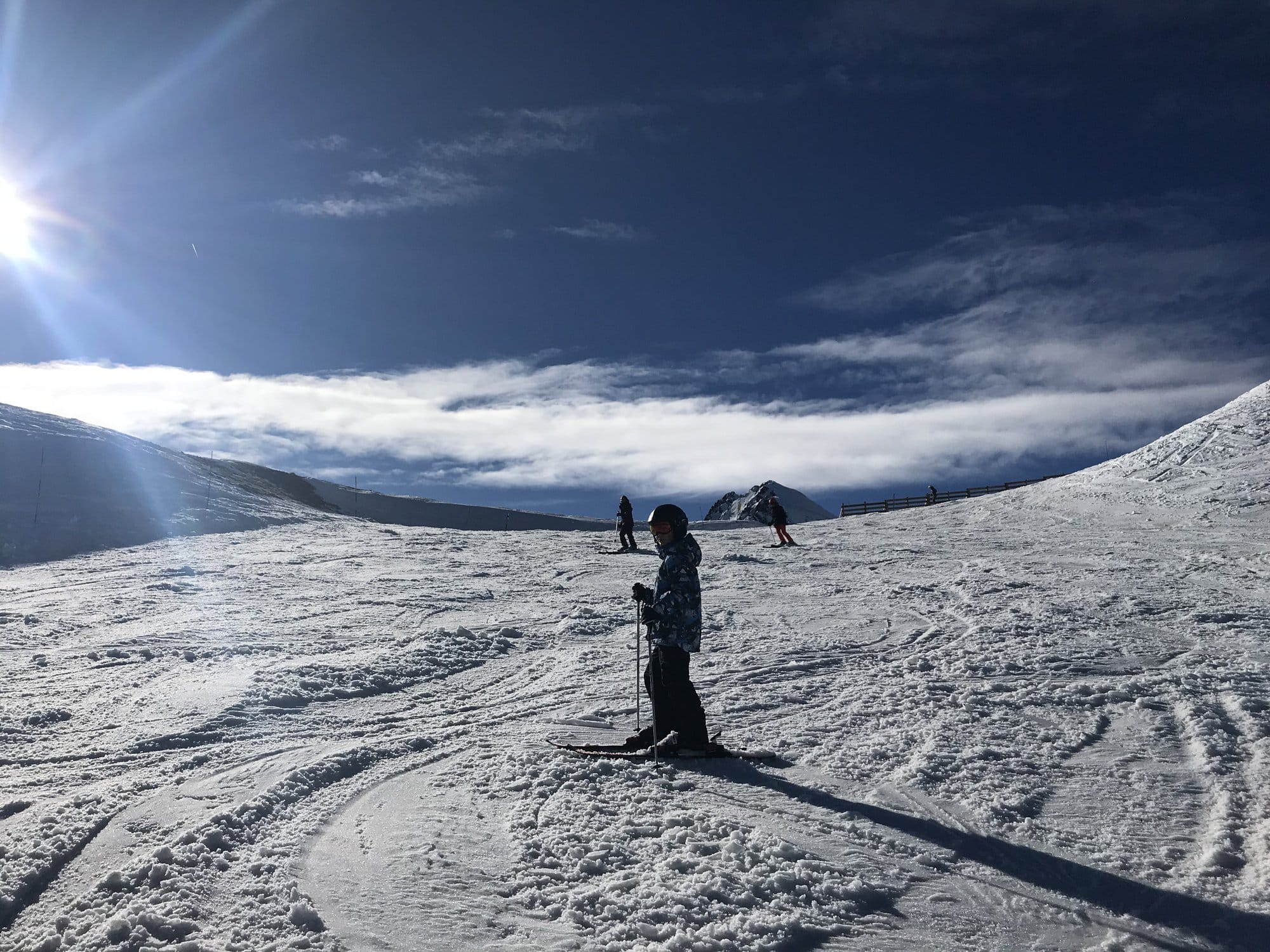 A child skiing in silhouette on an open piste with a dramatic sky, sea of clouds and Pyrenean peaks in the background — Cirque du Lys, Cauterets, France