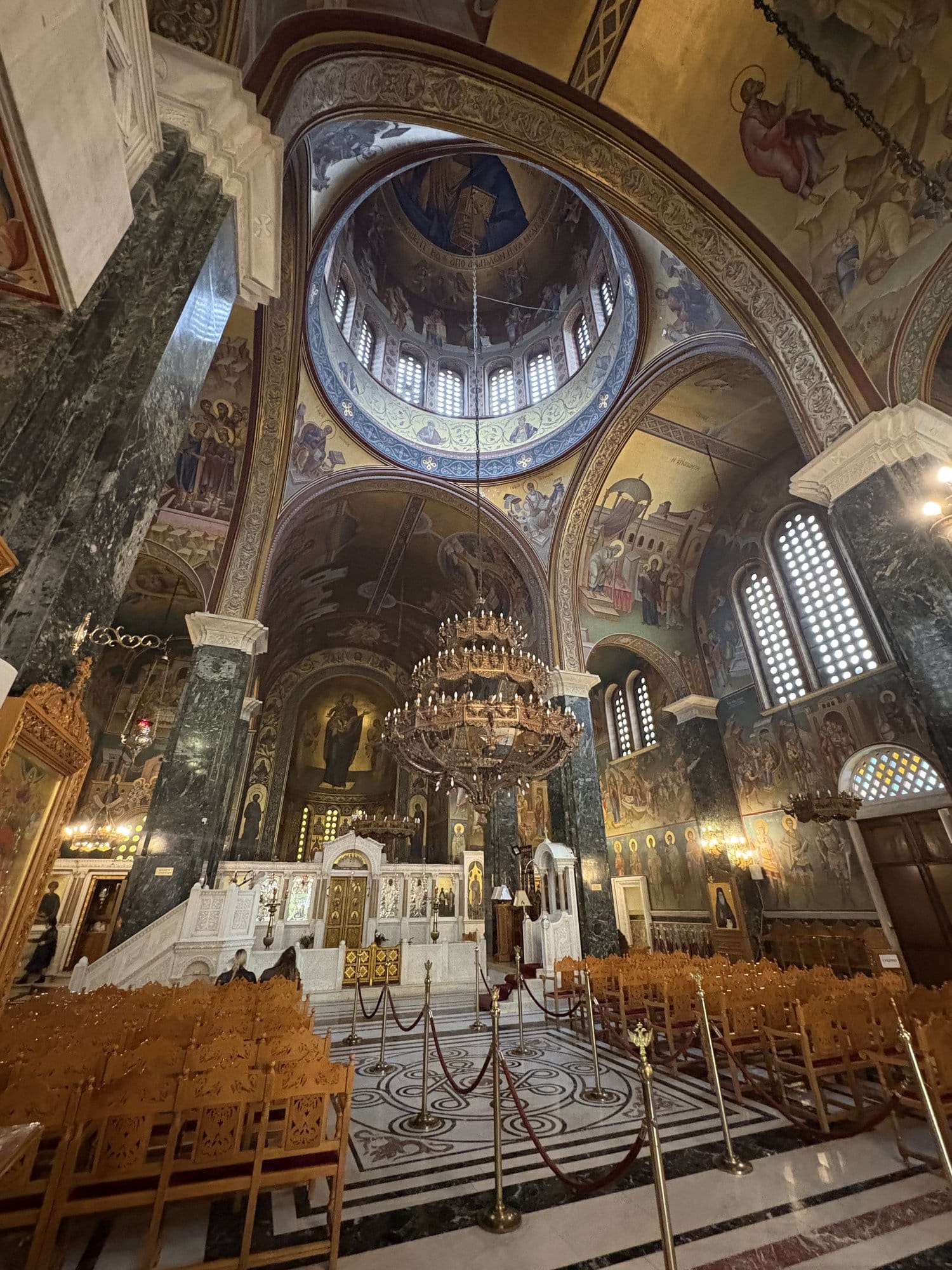 Intérieur d'une église orthodoxe à Thessalonique avec coupole peinte, lustres pendants, fresques et colonnes en marbre vert — Grèce