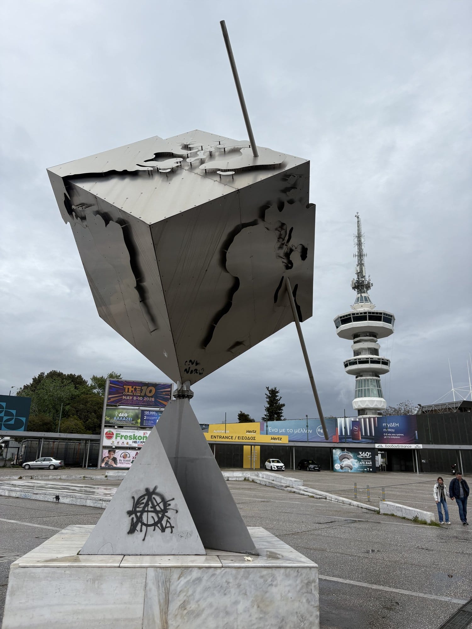 Sculpture moderne d'un globe en forme de cube avec la tour OTE derrière, dans le parc des expositions de Thessalonique — Grèce