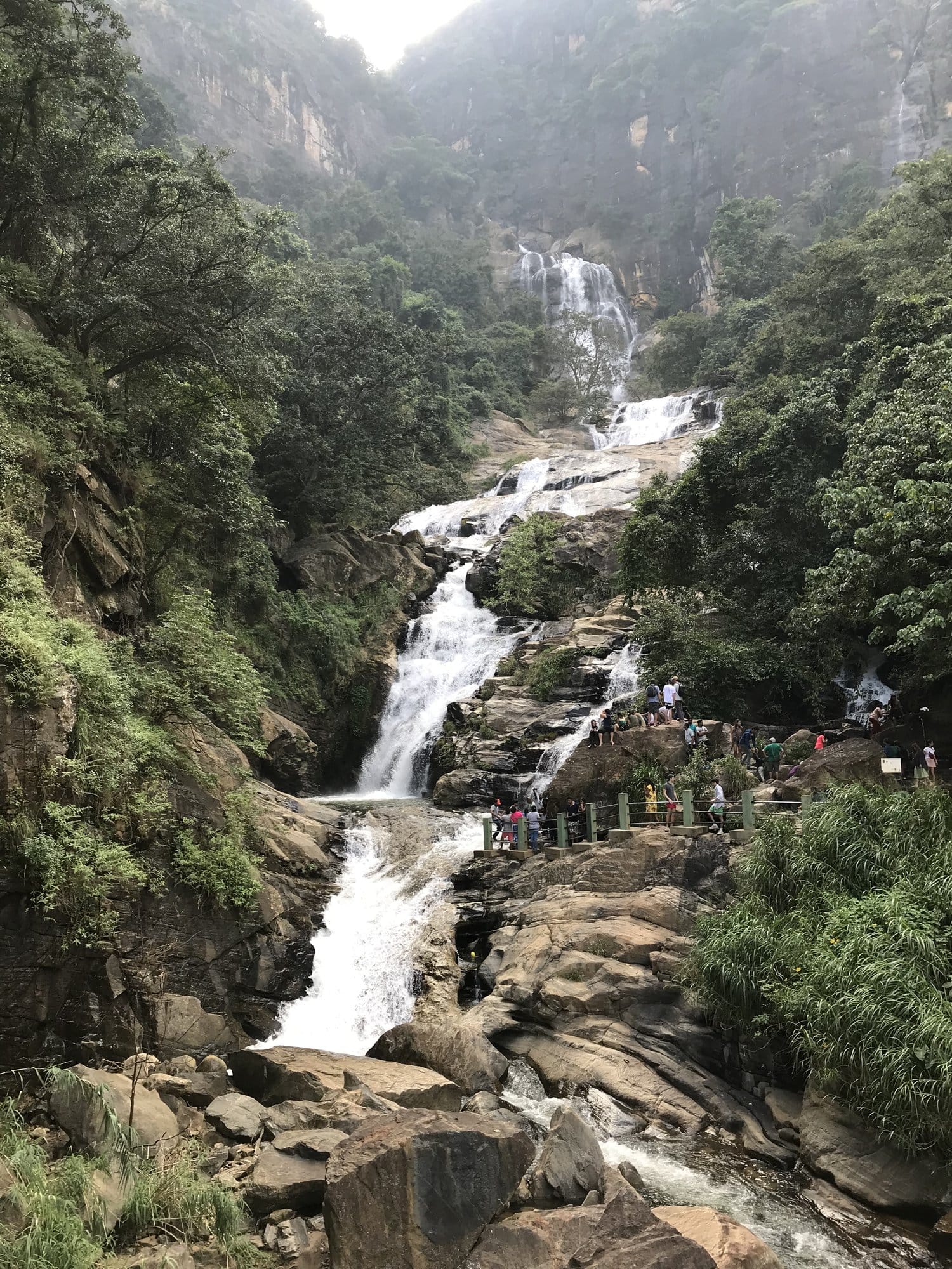 Dramatic waterfall cascading through a narrow gorge flanked by cliff walls and lush vegetation — Ravana Falls, Sri Lanka