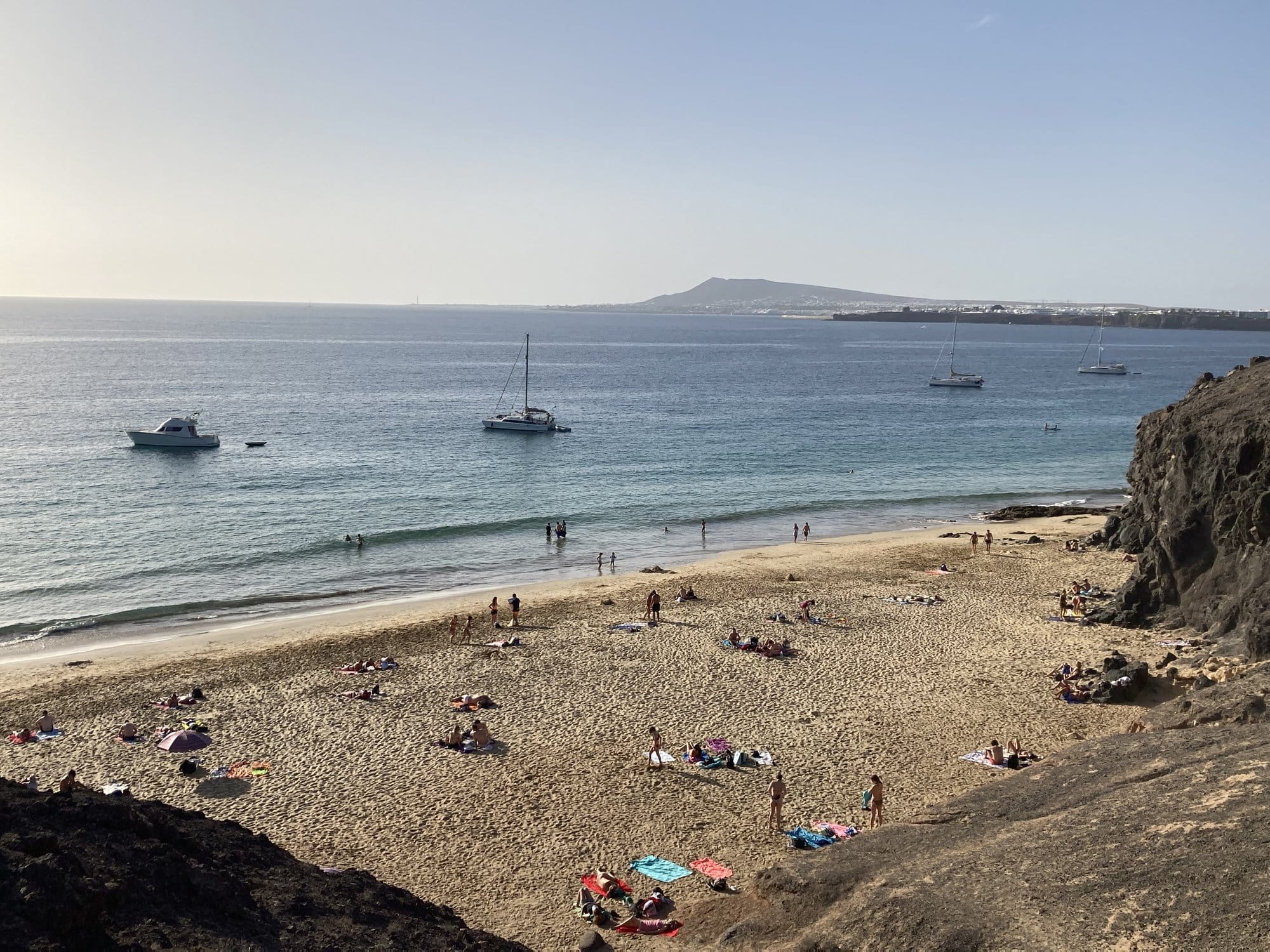 Playa Blanca beach with sunbathers, boats at anchor and the volcanic island of Fuerteventura visible across the strait — Lanzarote