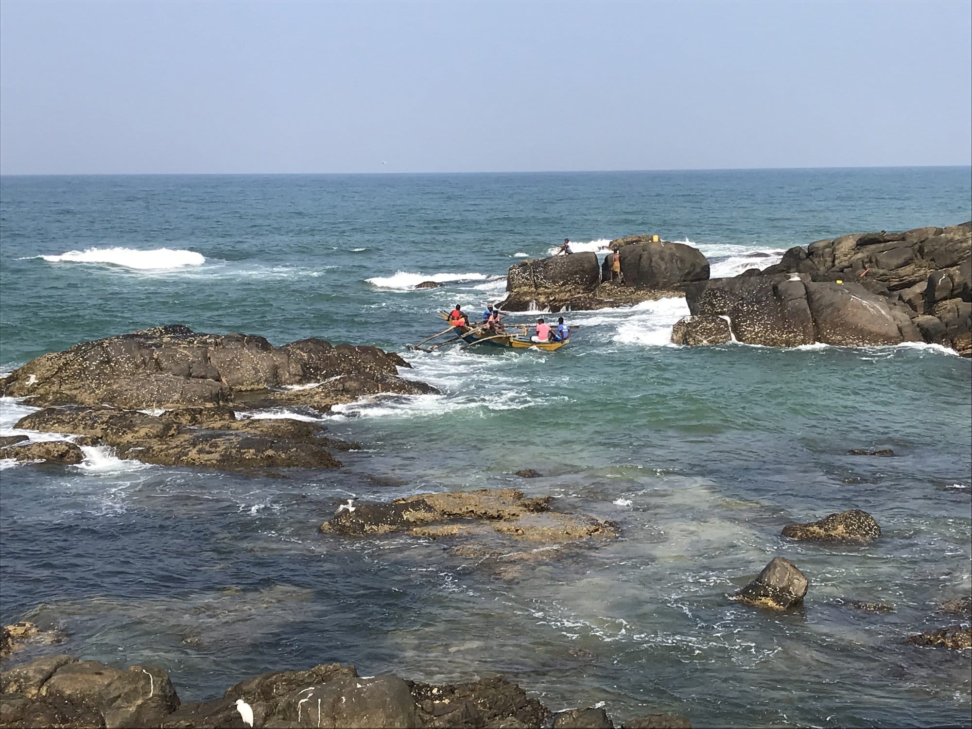 Rocky cove with rounded boulders in turquoise water and a small fishing boat — Ambalangoda, Sri Lanka
