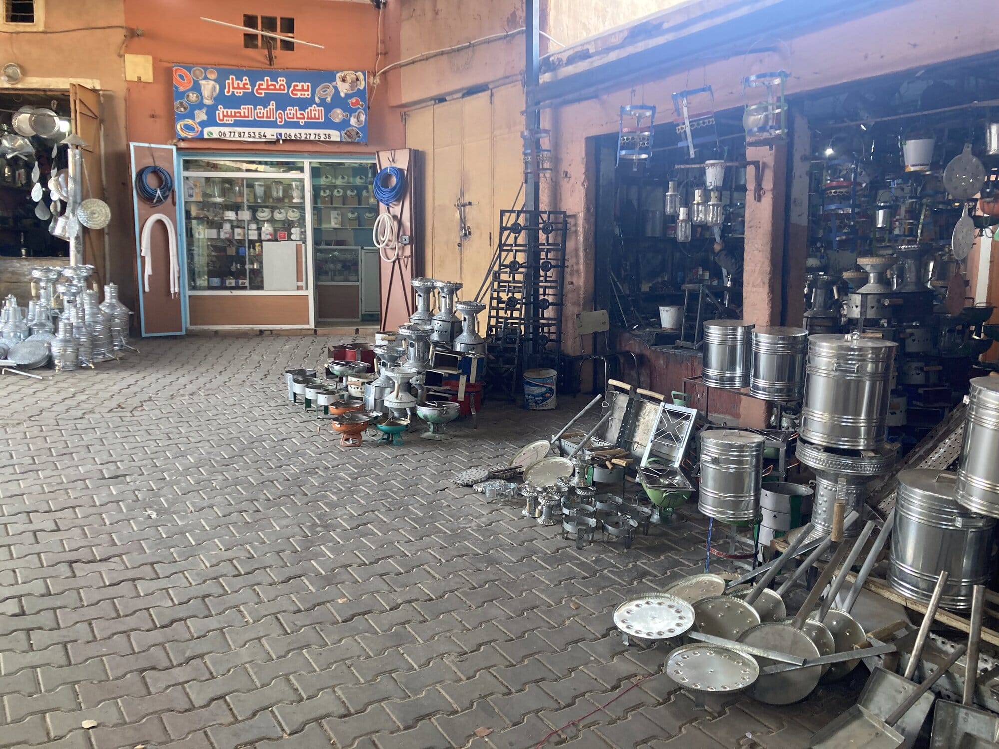 Ironmonger shop in the Tafraout souk — stacked aluminium tagines, lamps and cookware on the pavement — Tafraout, Morocco