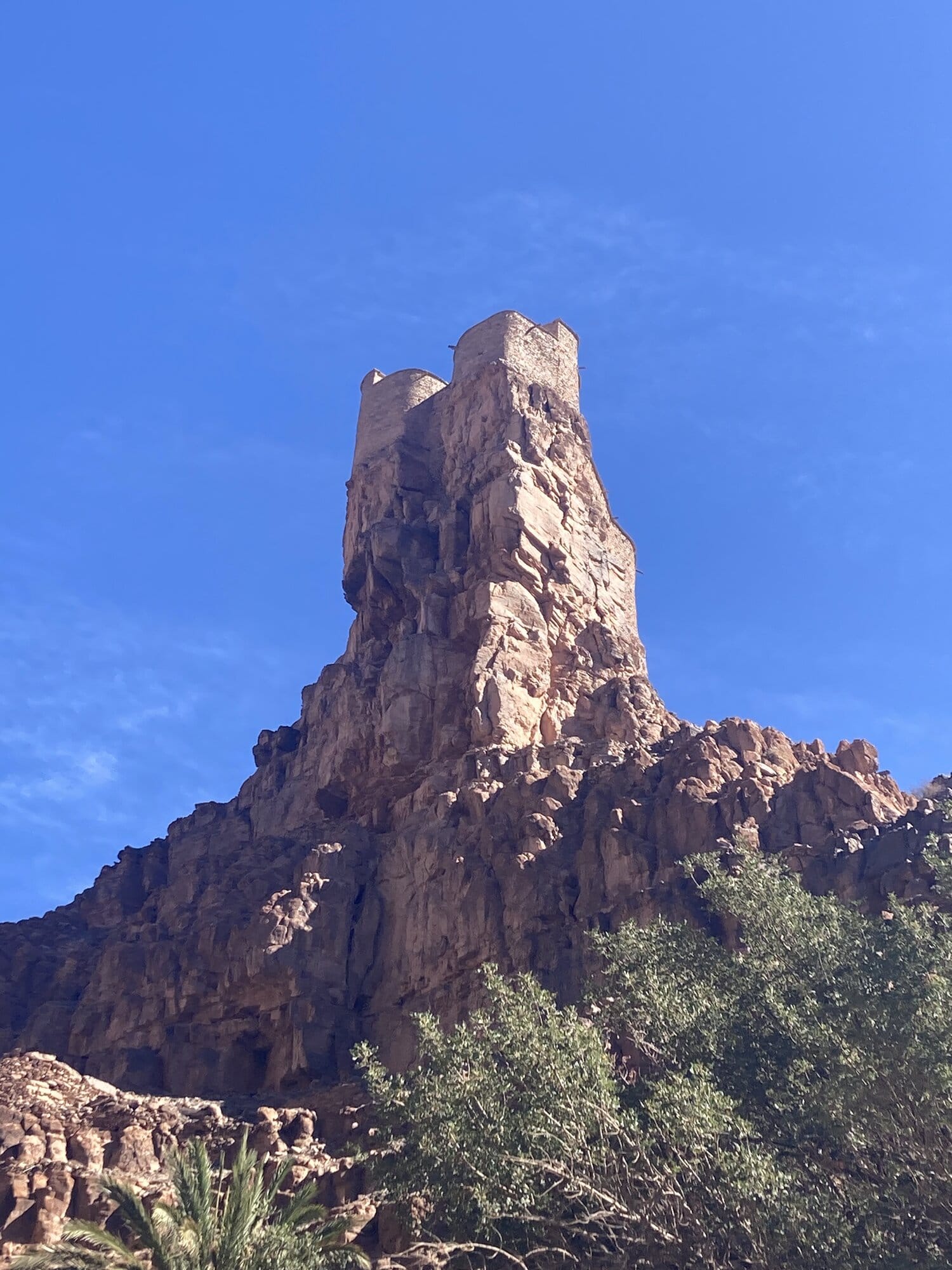 A shepherd in a brown djellaba leads his goats through a sunlit passage of the Aït Mansour canyon — Aït Mansour, Morocco