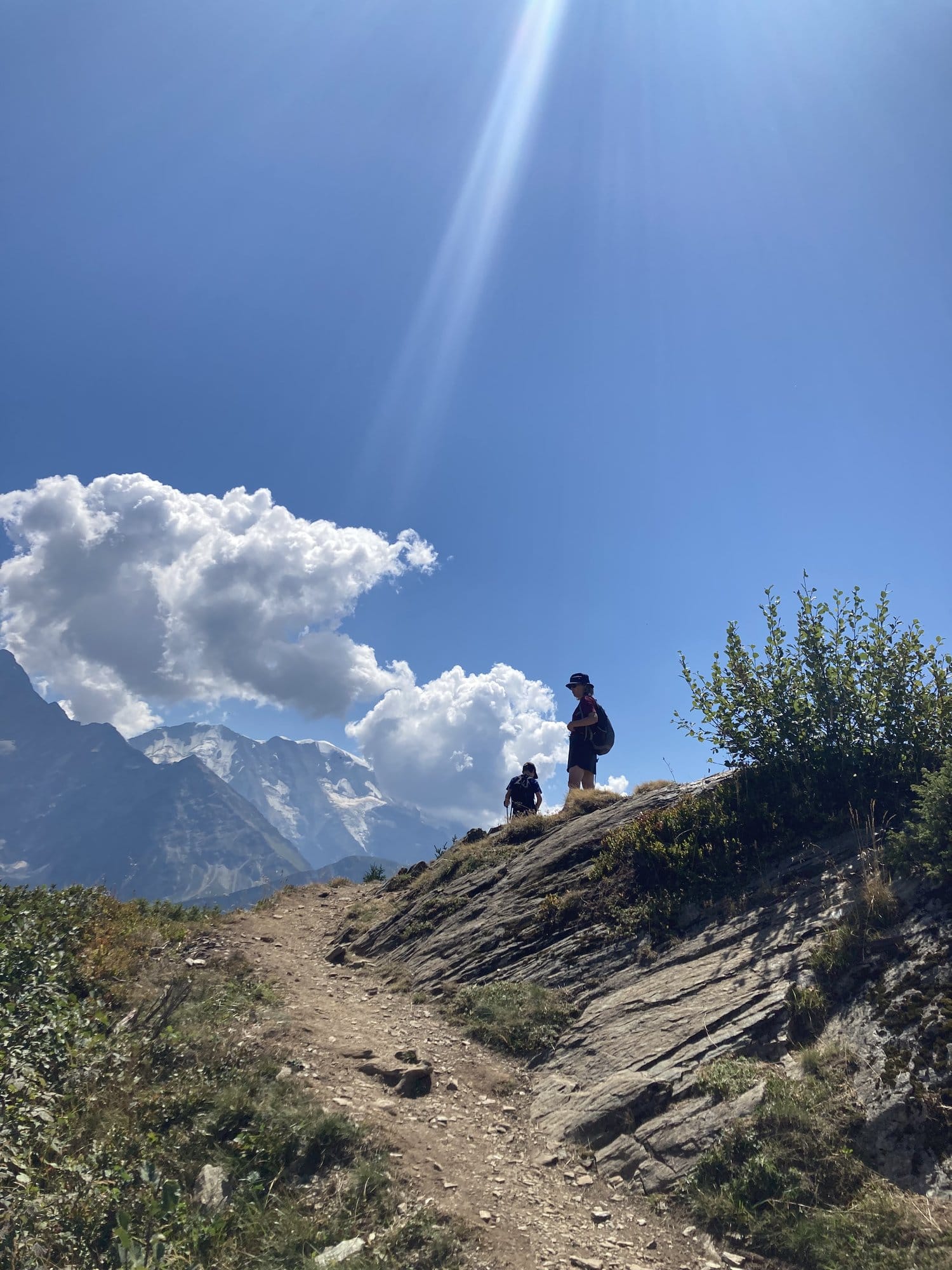 Two silhouettes standing on a rocky outcrop against the sky with the Mont-Blanc massif in the background, captured in backlight — Chamonix-Mont-Blanc, France