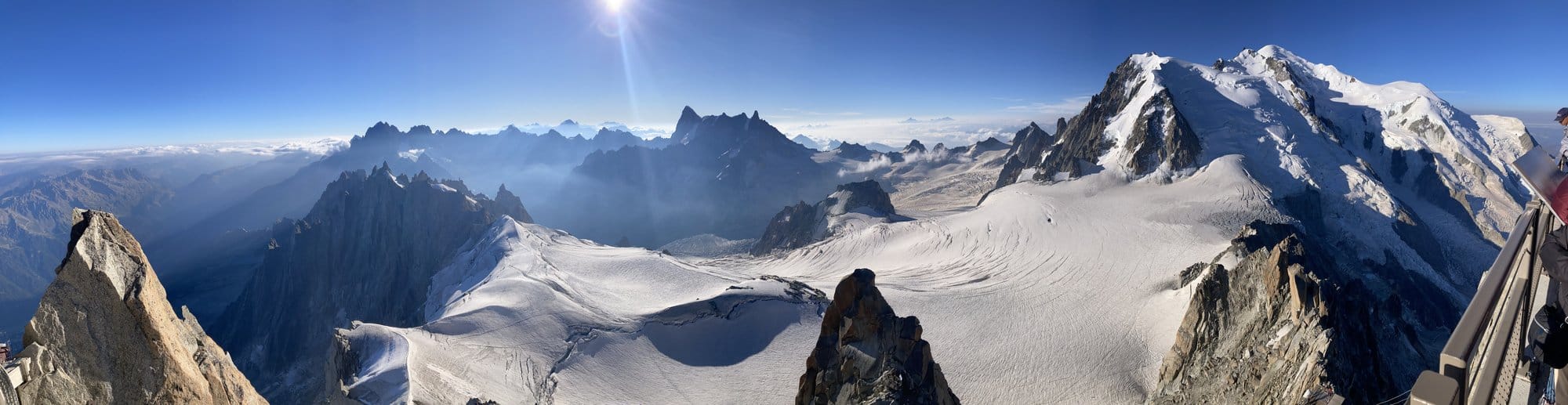 Panoramic view of the Mont-Blanc massif from the Aiguille du Midi summit terrace at 3,816m, with glaciers, granite peaks, and a sea of clouds on the horizon — Chamonix-Mont-Blanc, France