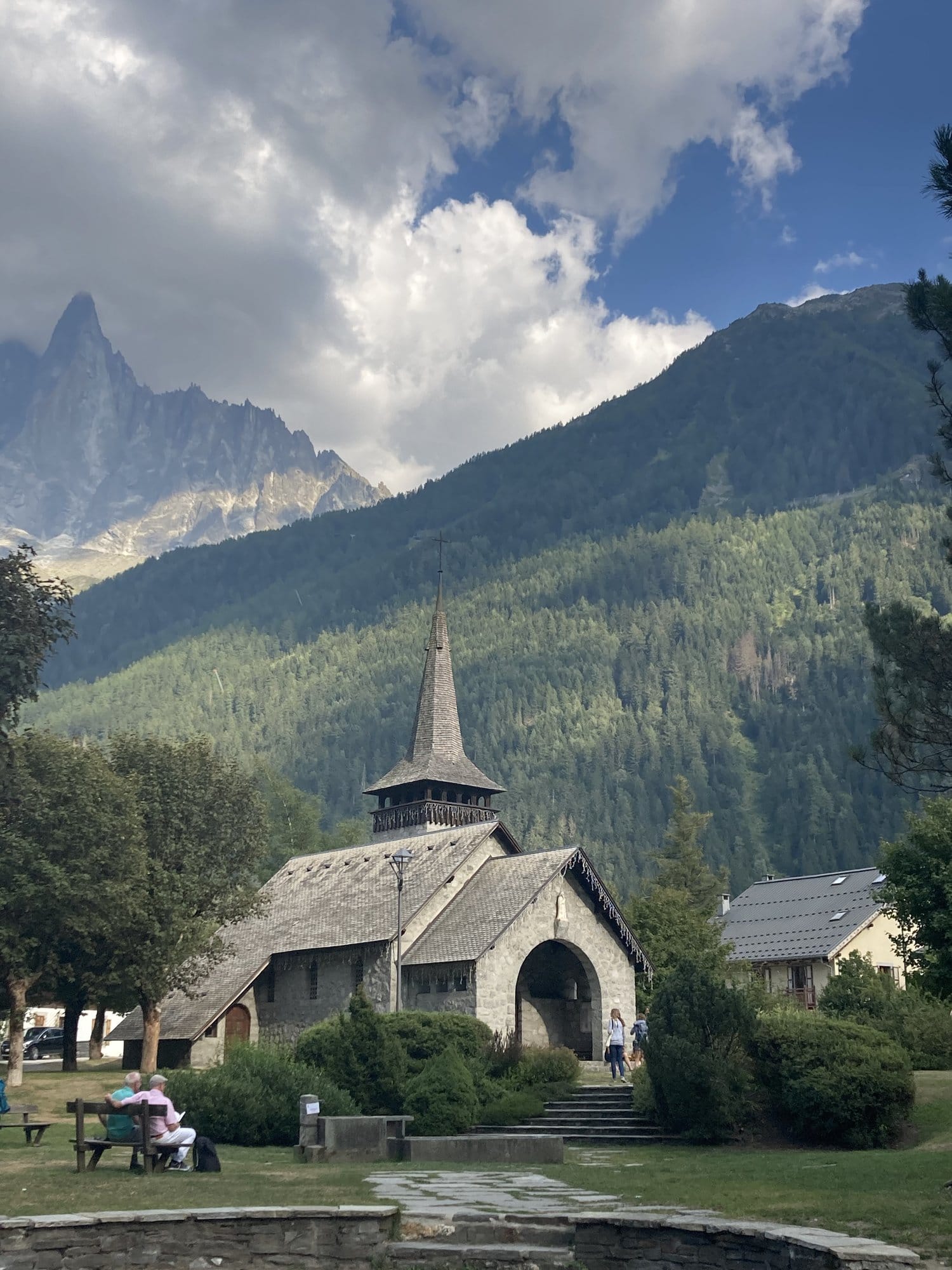 Small stone chapel with a wooden bell tower at Les Praz-de-Chamonix, with the dramatic Aiguille des Drus rising behind it — Chamonix-Mont-Blanc, France