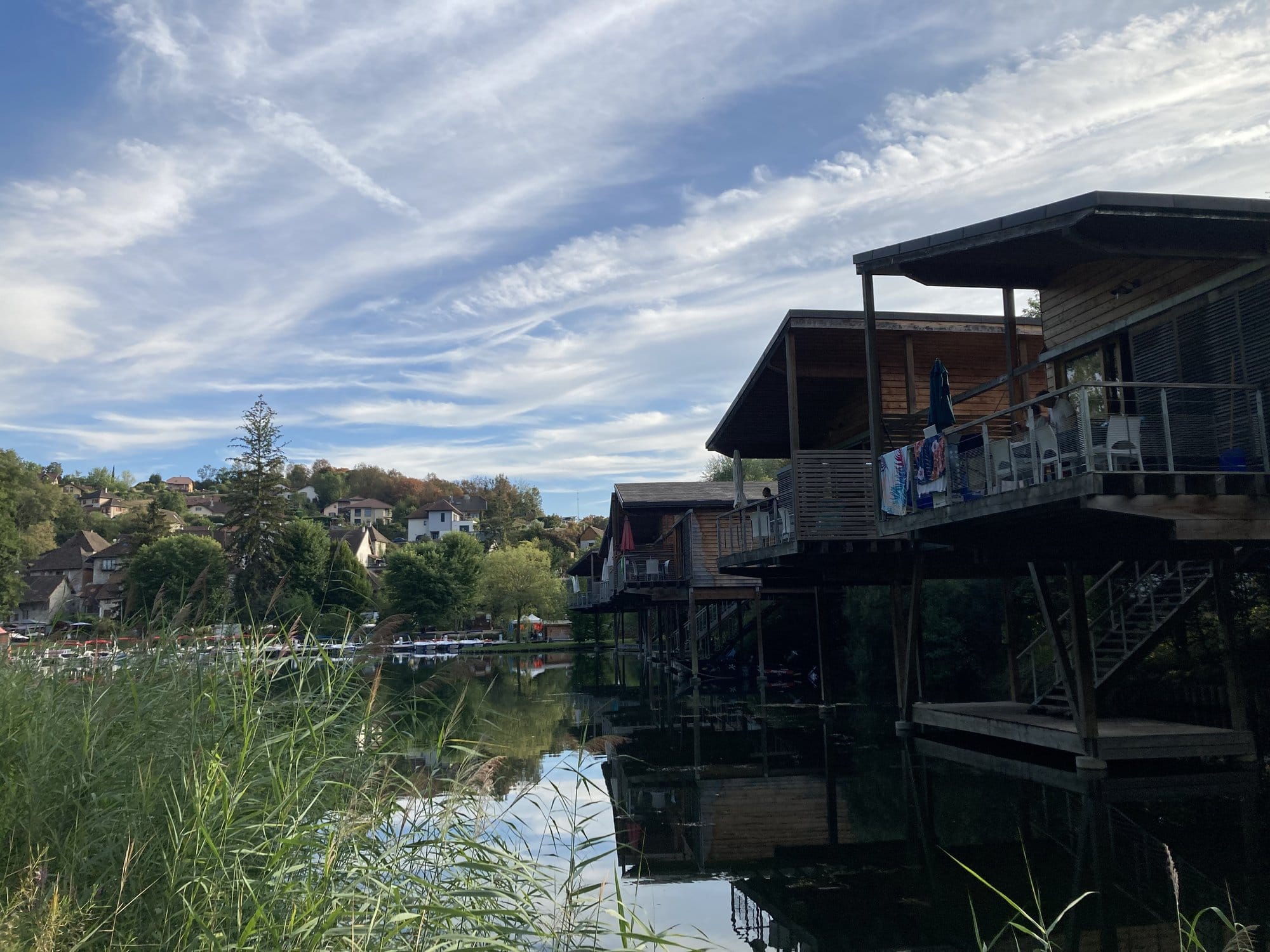 Wooden lakeside terraces and restaurant extending over calm water at sunset, with reeds in the foreground — Lac du Bourget, France