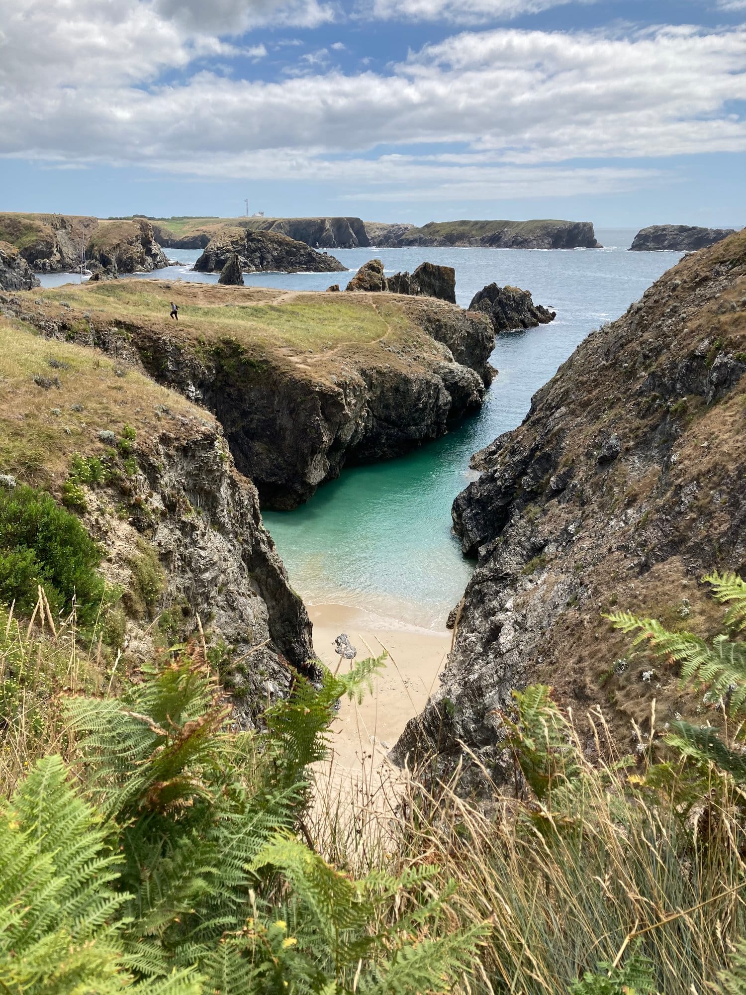 A secret cove revealed through a narrow gap in the cliffs, turquoise water catching the light, a solitary figure on the tiny beach below