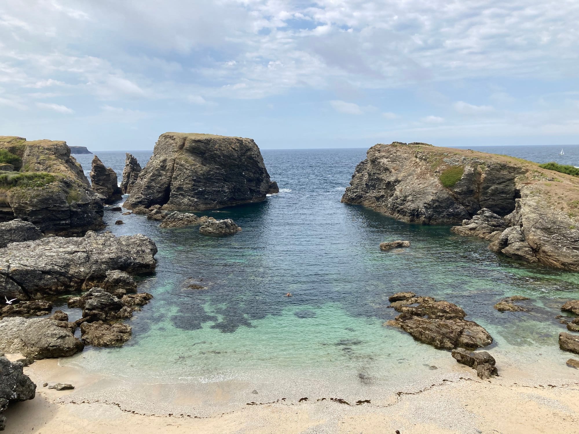 A sandy beach cove framed by two massive granite rock stacks, crystal-clear water in the channel between them