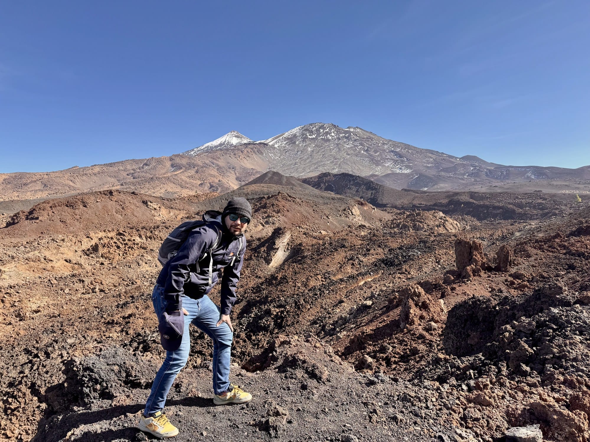 The snow-capped twin summits of Teide and Pico Viejo seen from the red volcanic slopes of Montaña Samara — Teide National Park, Tenerife